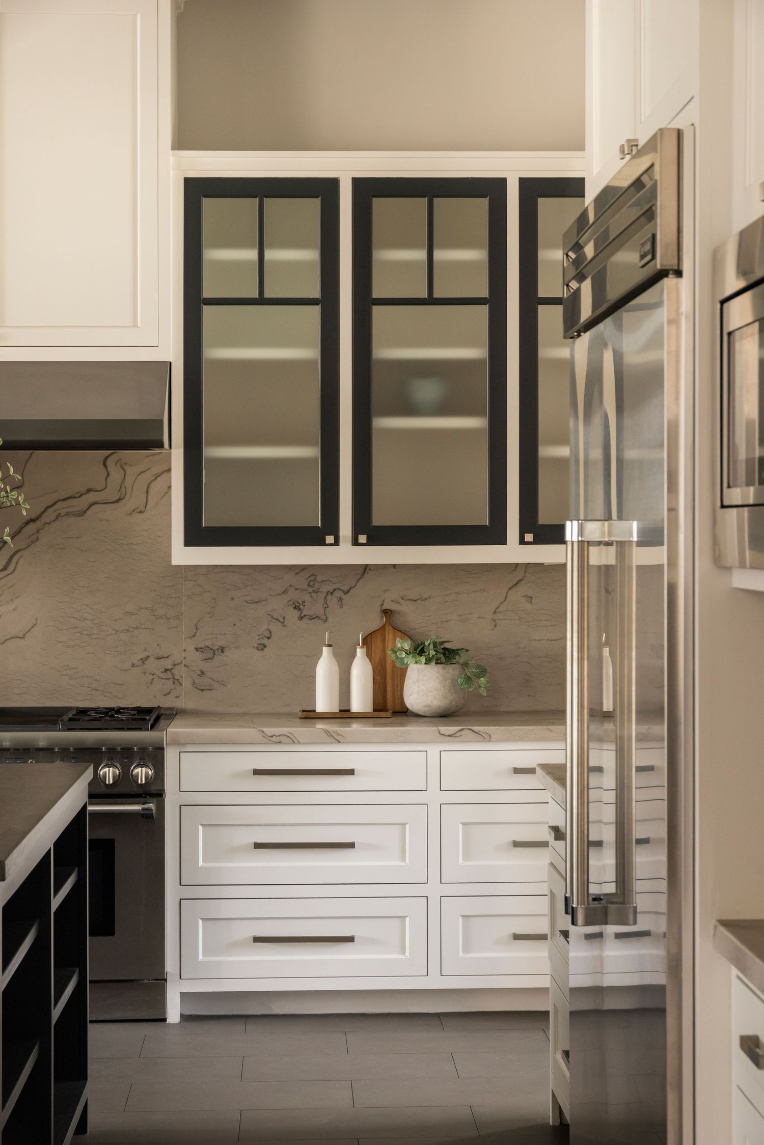 White kitchen cabinets with black glass doors and marble-look backsplash.