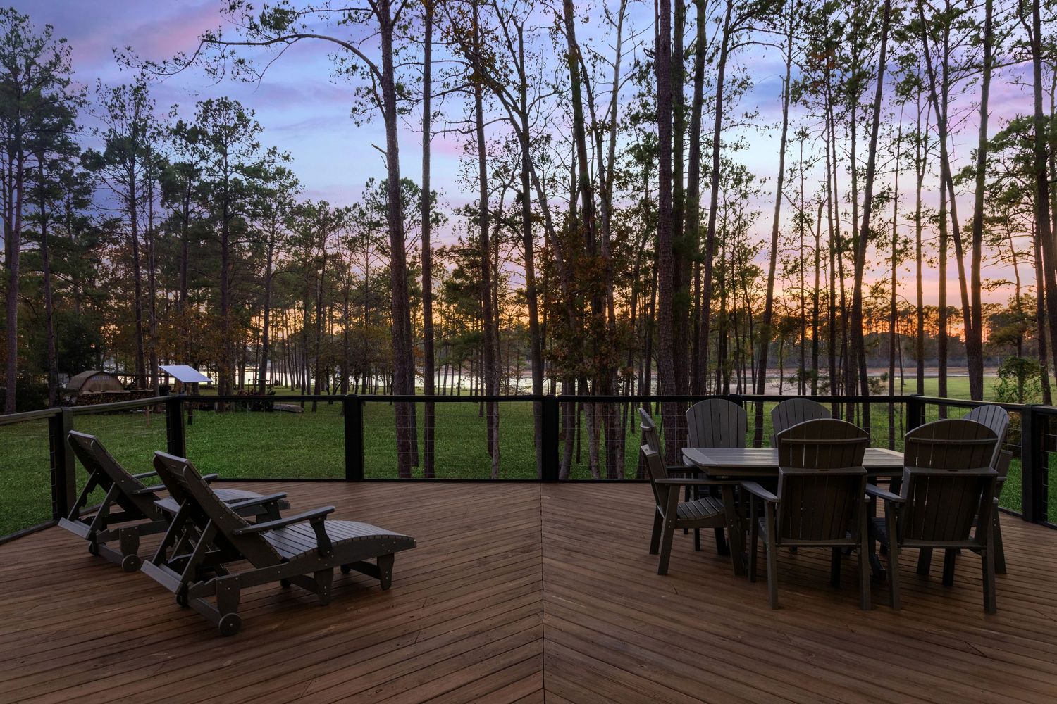 Spacious wooden deck with outdoor furniture overlooking pine forest at sunset.