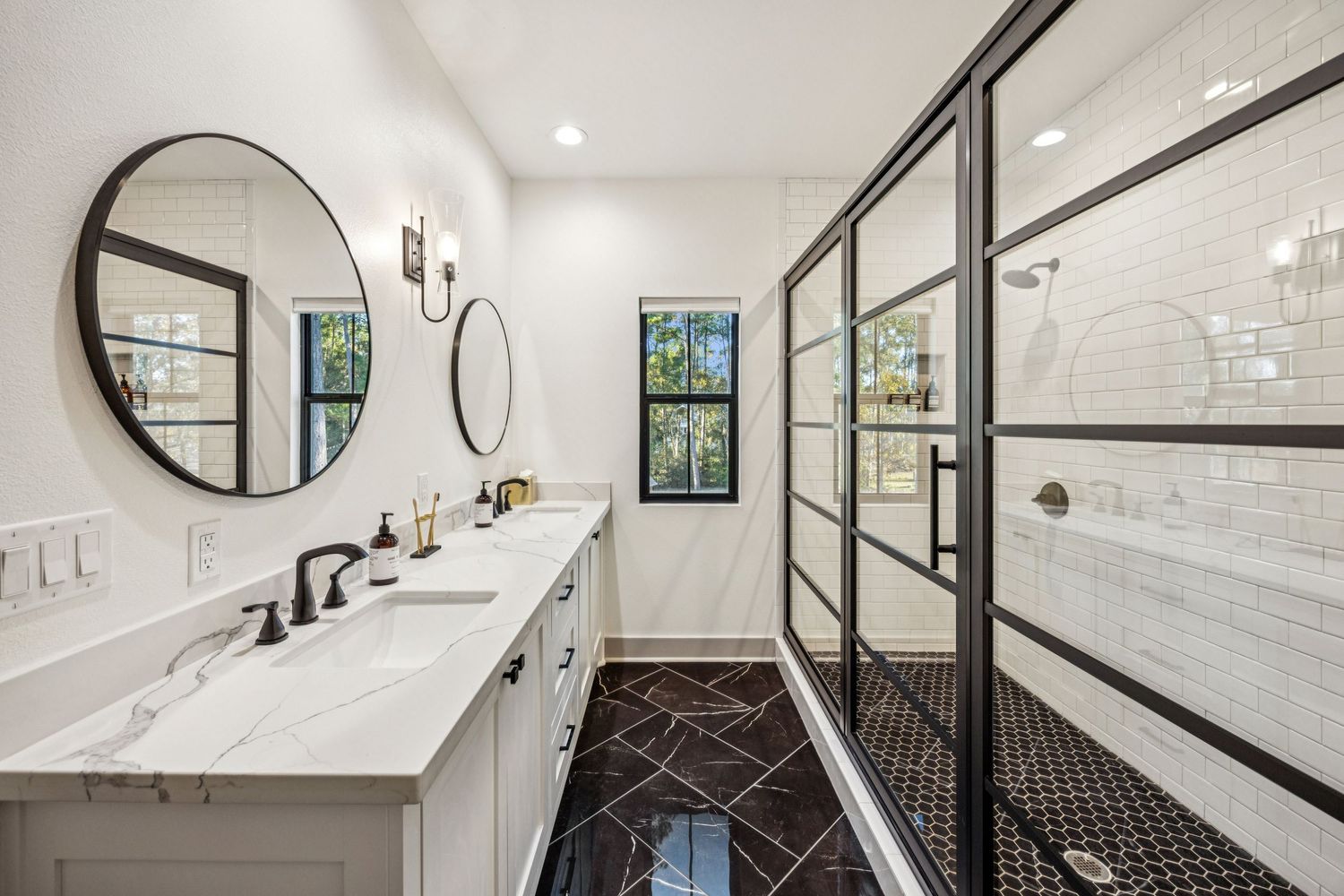 Modern bathroom with white vanity, circular mirror, and black geometric floor tile pattern.