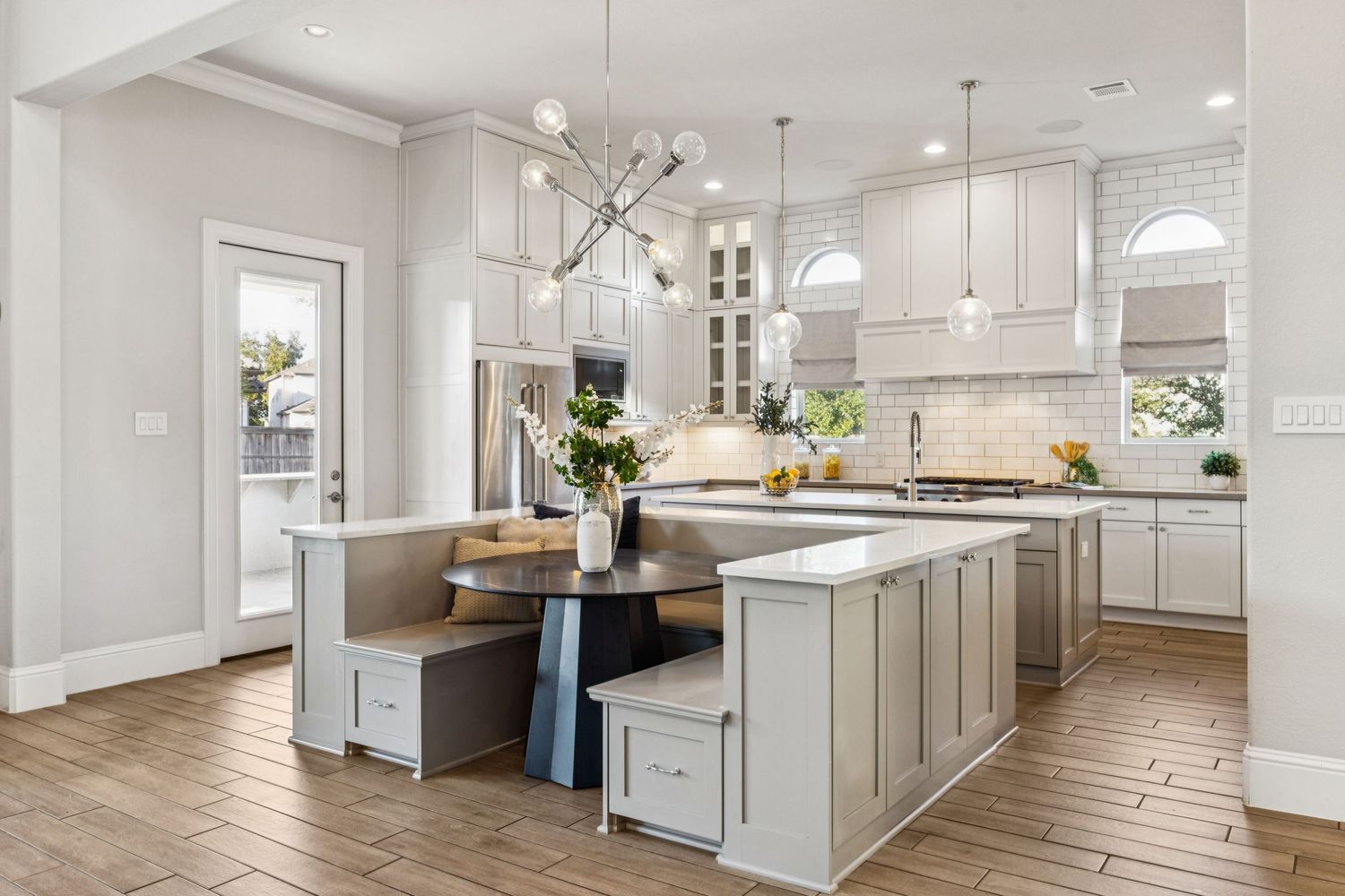 Modern open concept kitchen and living area with white cabinets, hardwood floors, and natural lighting.