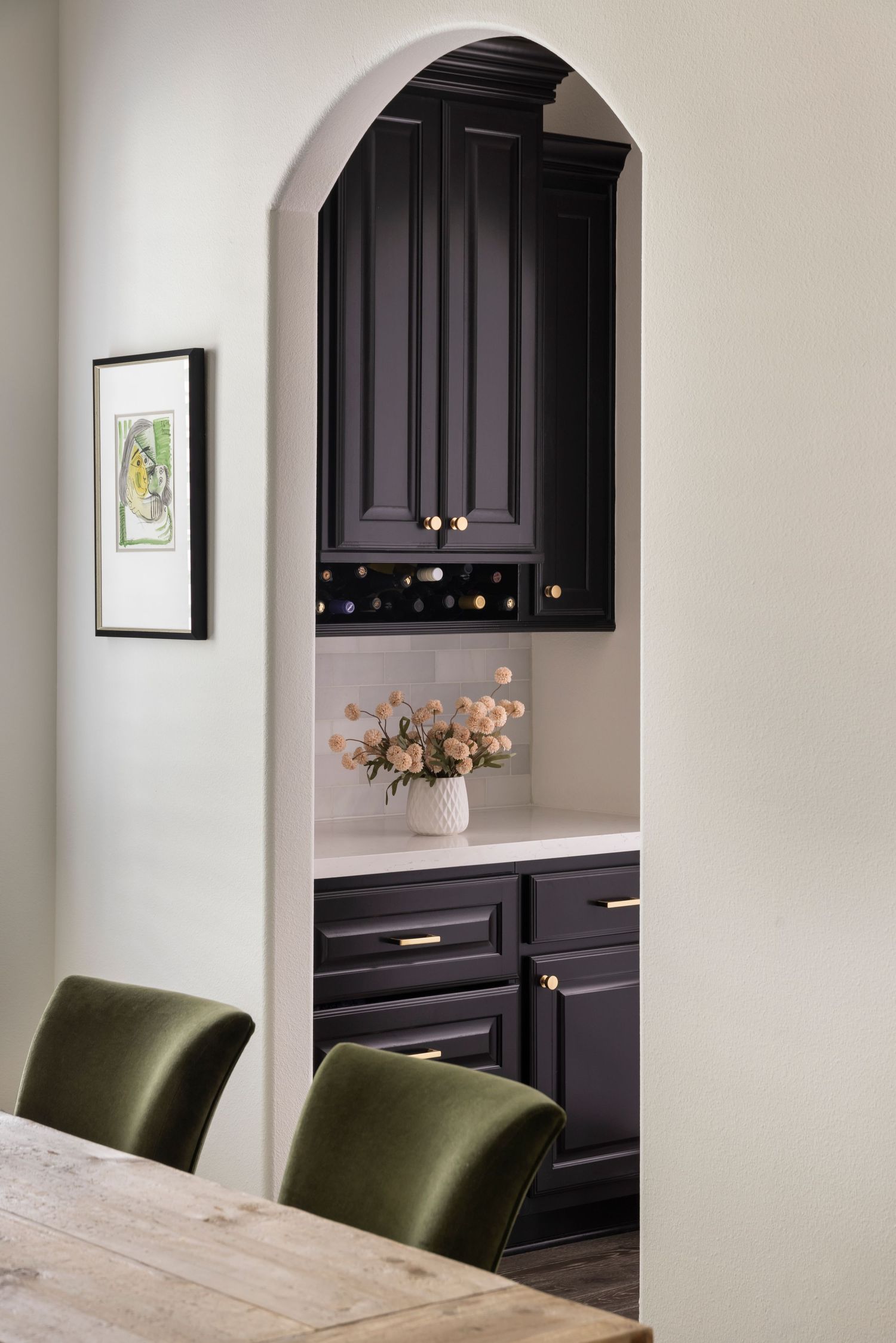 Modern kitchen design featuring black built-in cabinets with brass hardware and olive green velvet dining chairs.