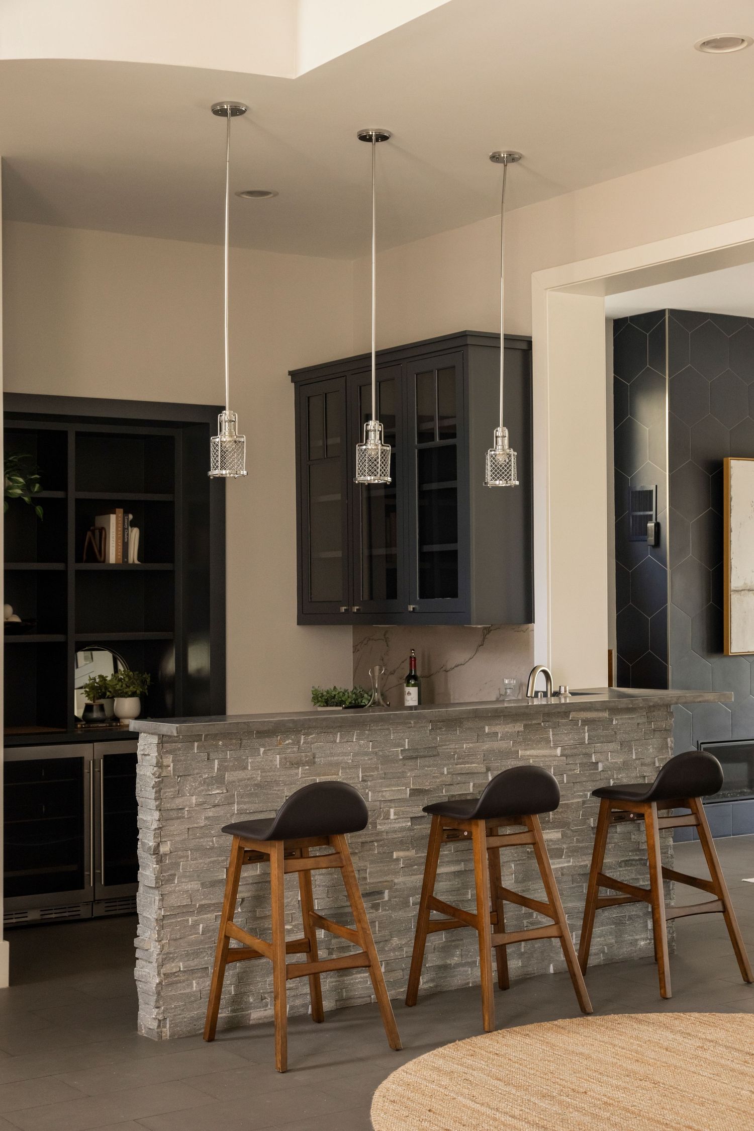 Modern kitchen bar with wooden stools, pendant lights, and stone accent wall.