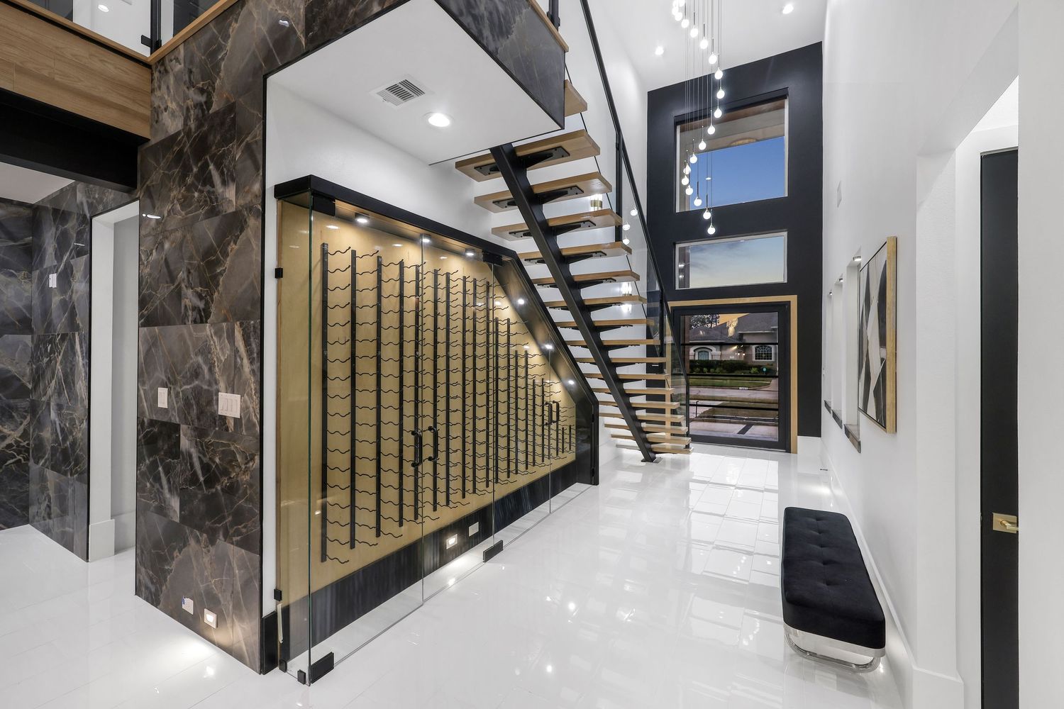 Elegant hallway with floating staircase and illuminated wine wall storage featuring marble accents.