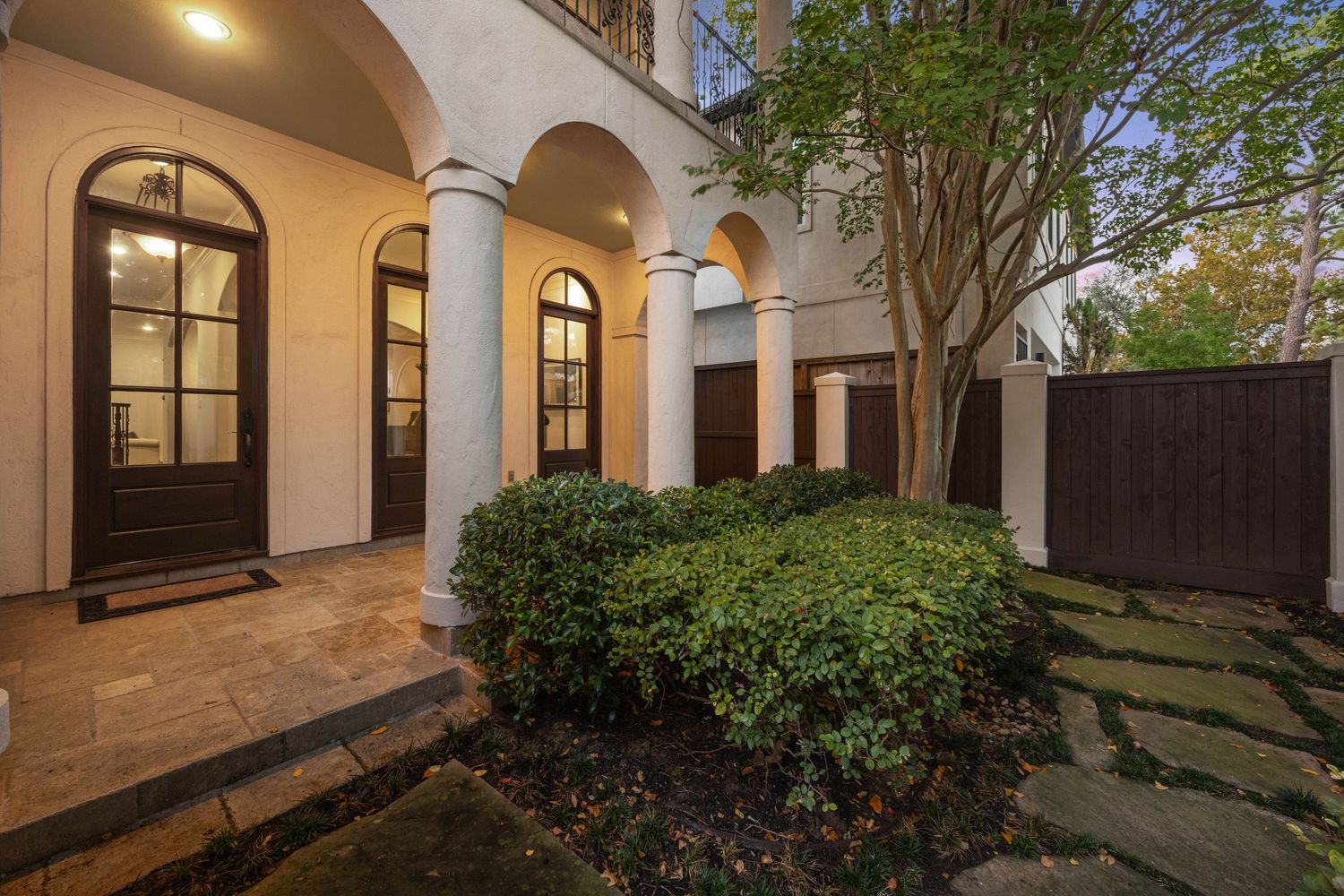 Elegant Mediterranean-style home exterior with arched walkways and landscaped courtyard illuminated at dusk.