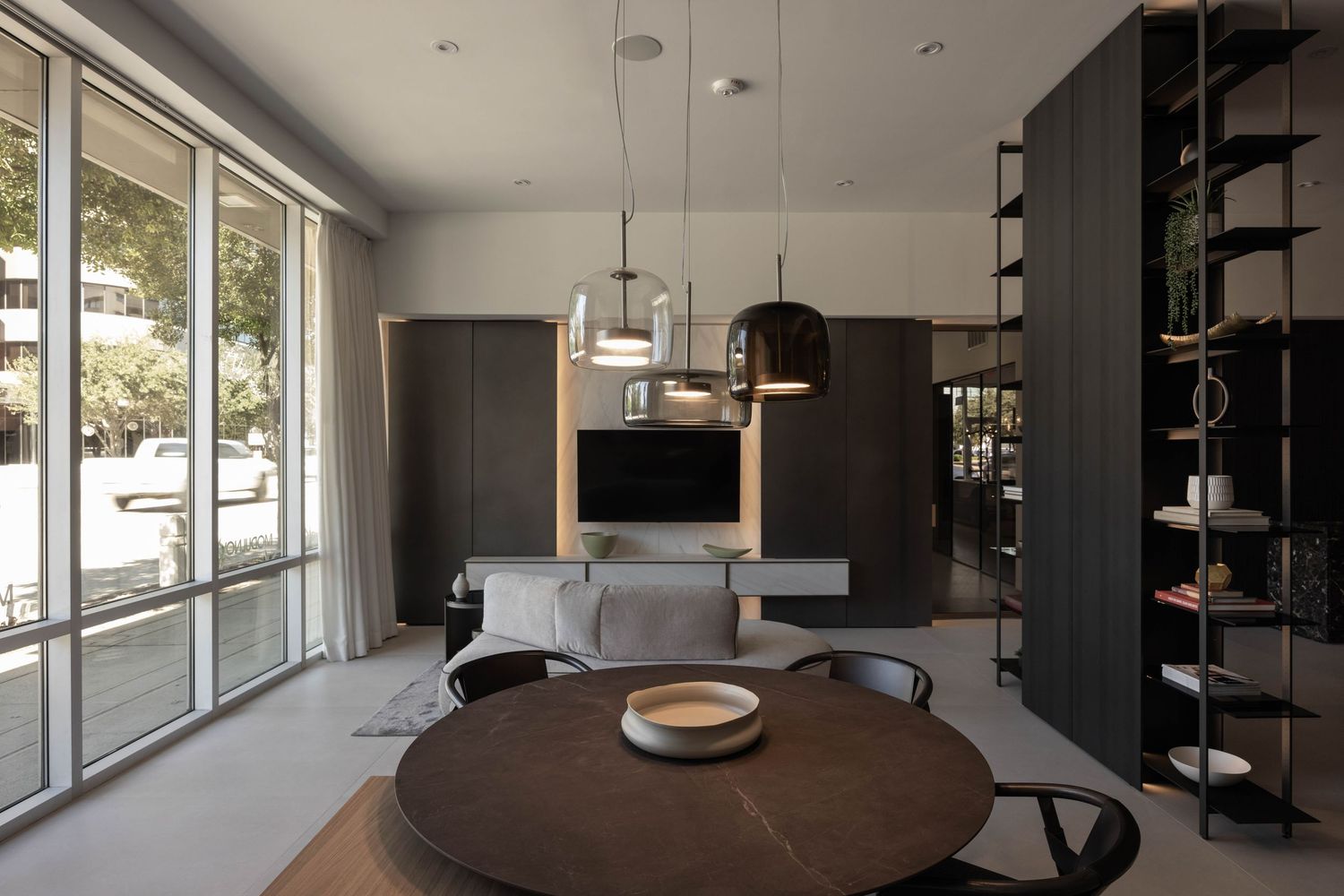 Modern minimalist living room with large windows, dark furniture, and natural lighting.