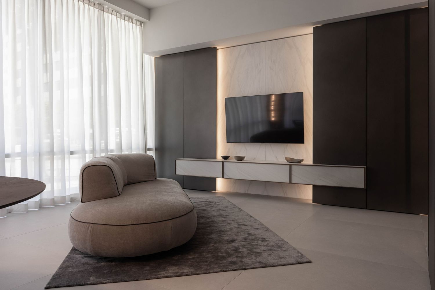 Contemporary living room with curved sofa and sheer curtains in neutral colors.