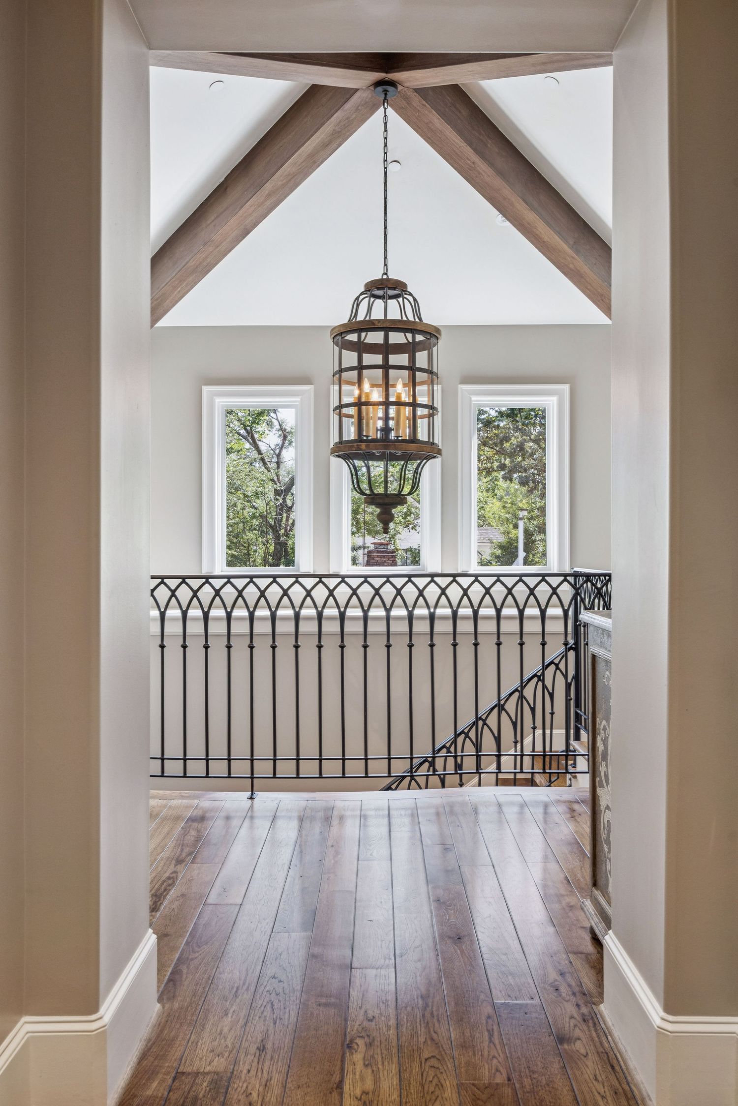 Upper level landing with vaulted ceilings, wooden beams, and wrought iron railings.