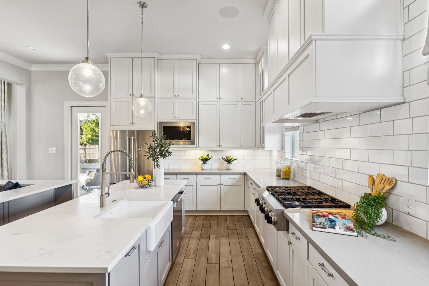 Bright white modern kitchen with subway tile backsplash and hardwood flooring.
