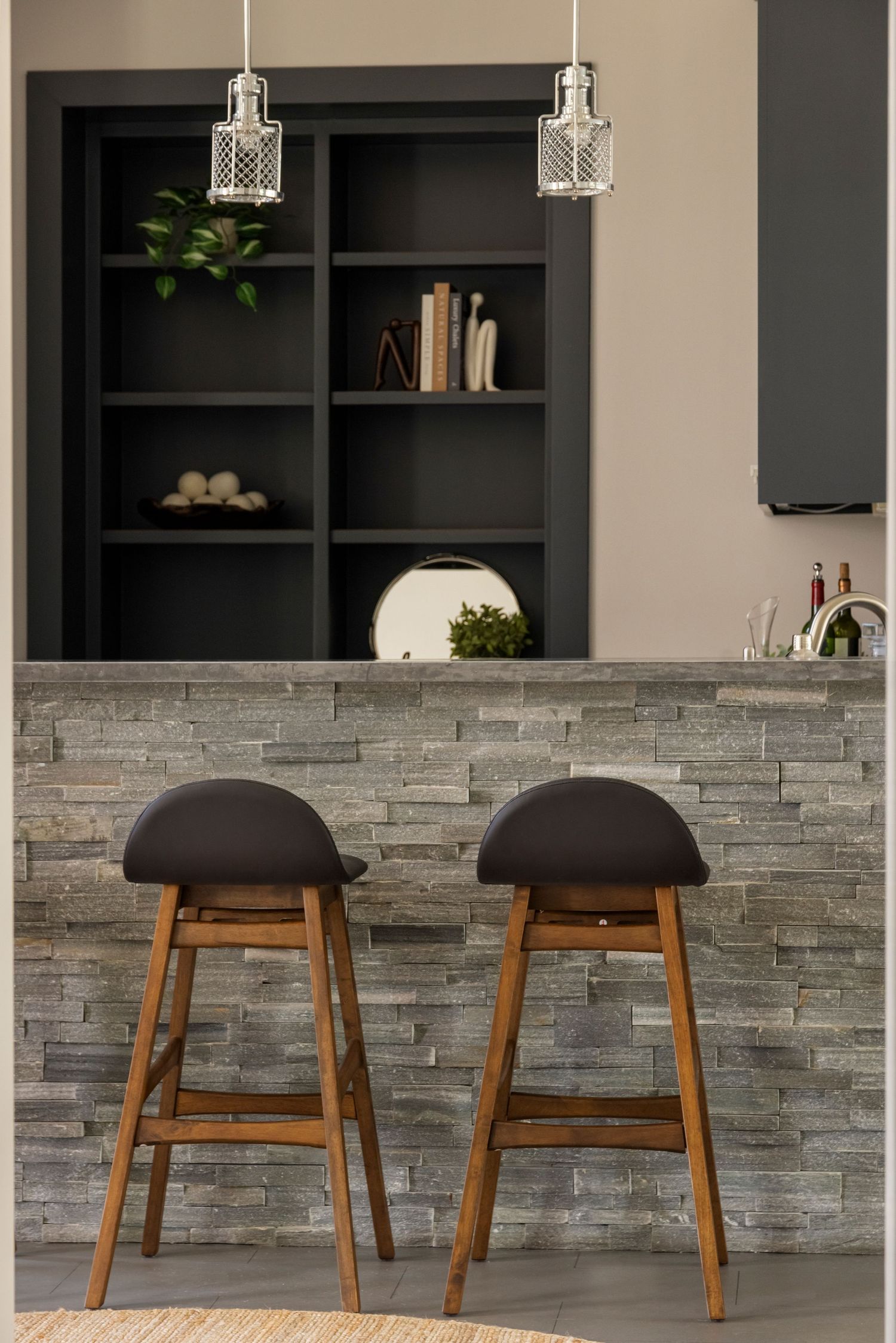 Modern bar area with wooden stools, stone accent wall, and geometric pendant lights.