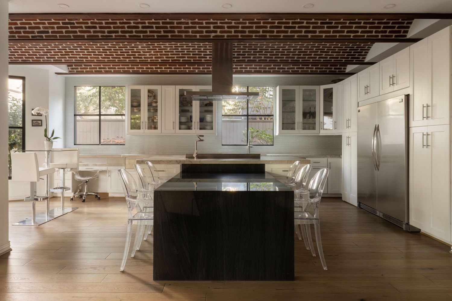 Long view of modern kitchen with exposed brick ceiling and sleek white cabinetry.