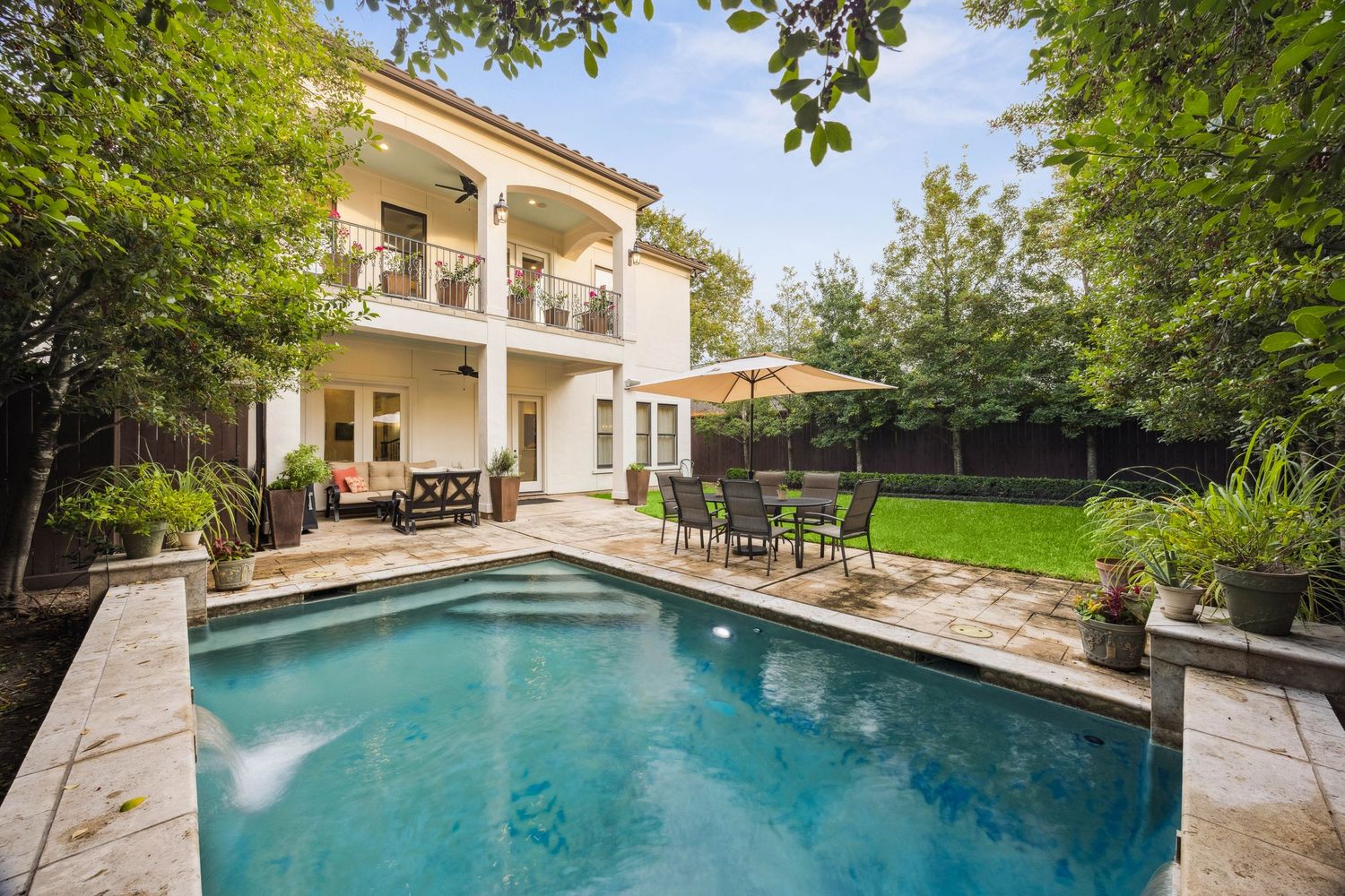 Backyard oasis featuring a large swimming pool, stone patio, and lush landscaping.