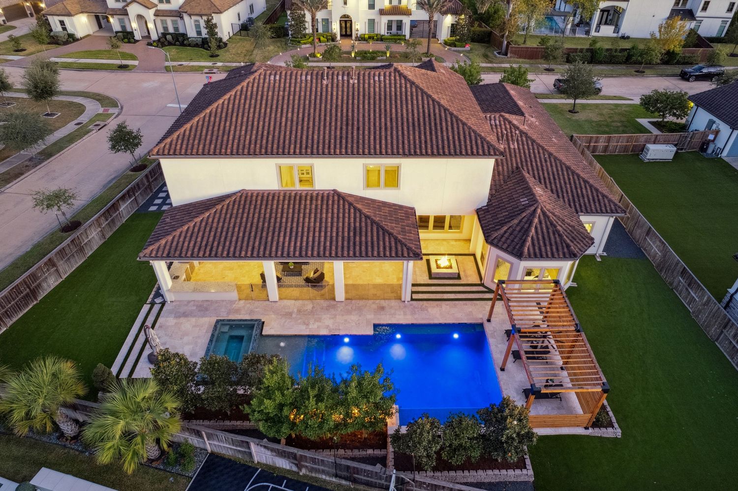 Twilight aerial view of luxury estate with illuminated pool and landscaped grounds.