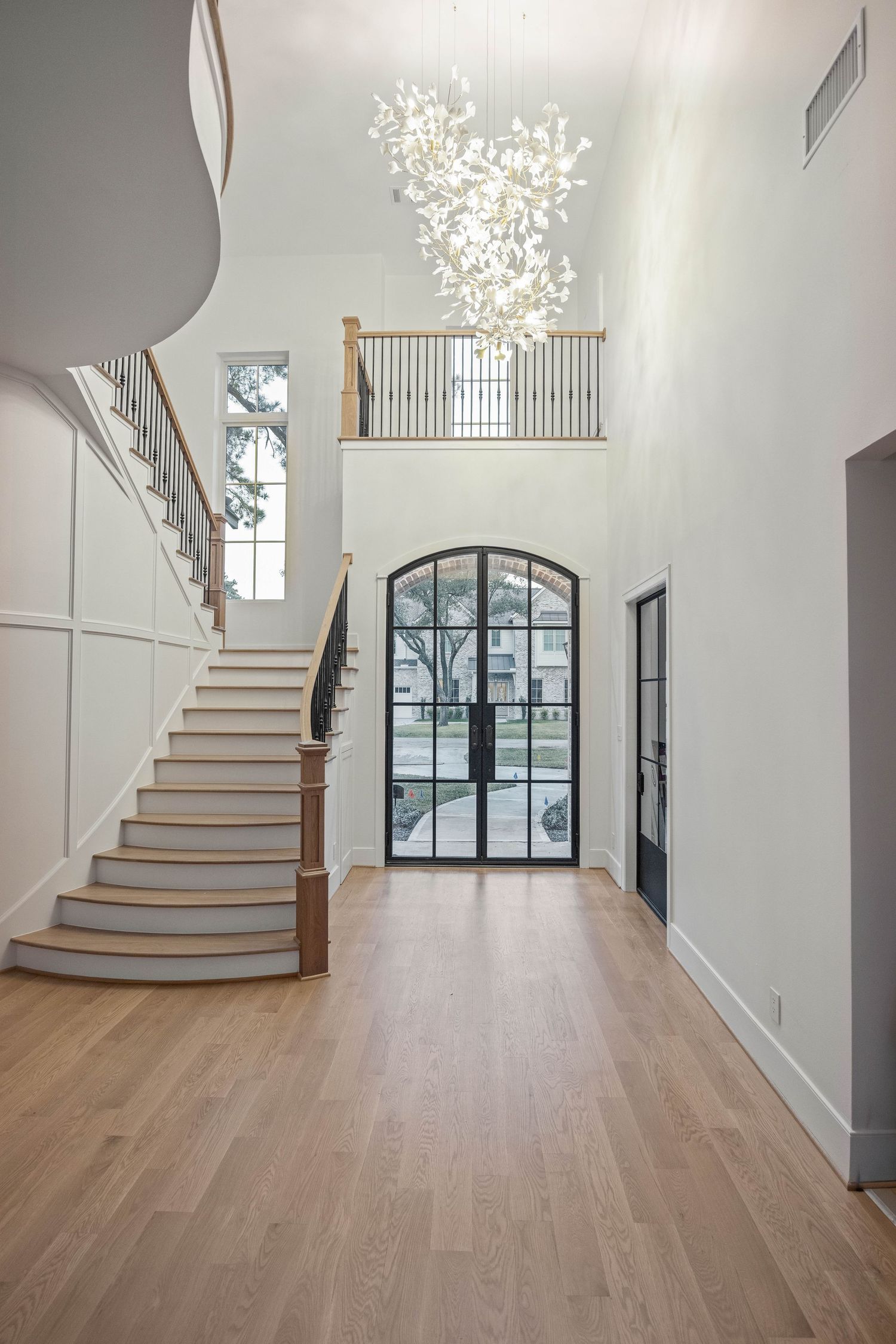 Modern interior hallway with curved wooden staircase, hardwood floors, and elegant chandelier lighting.