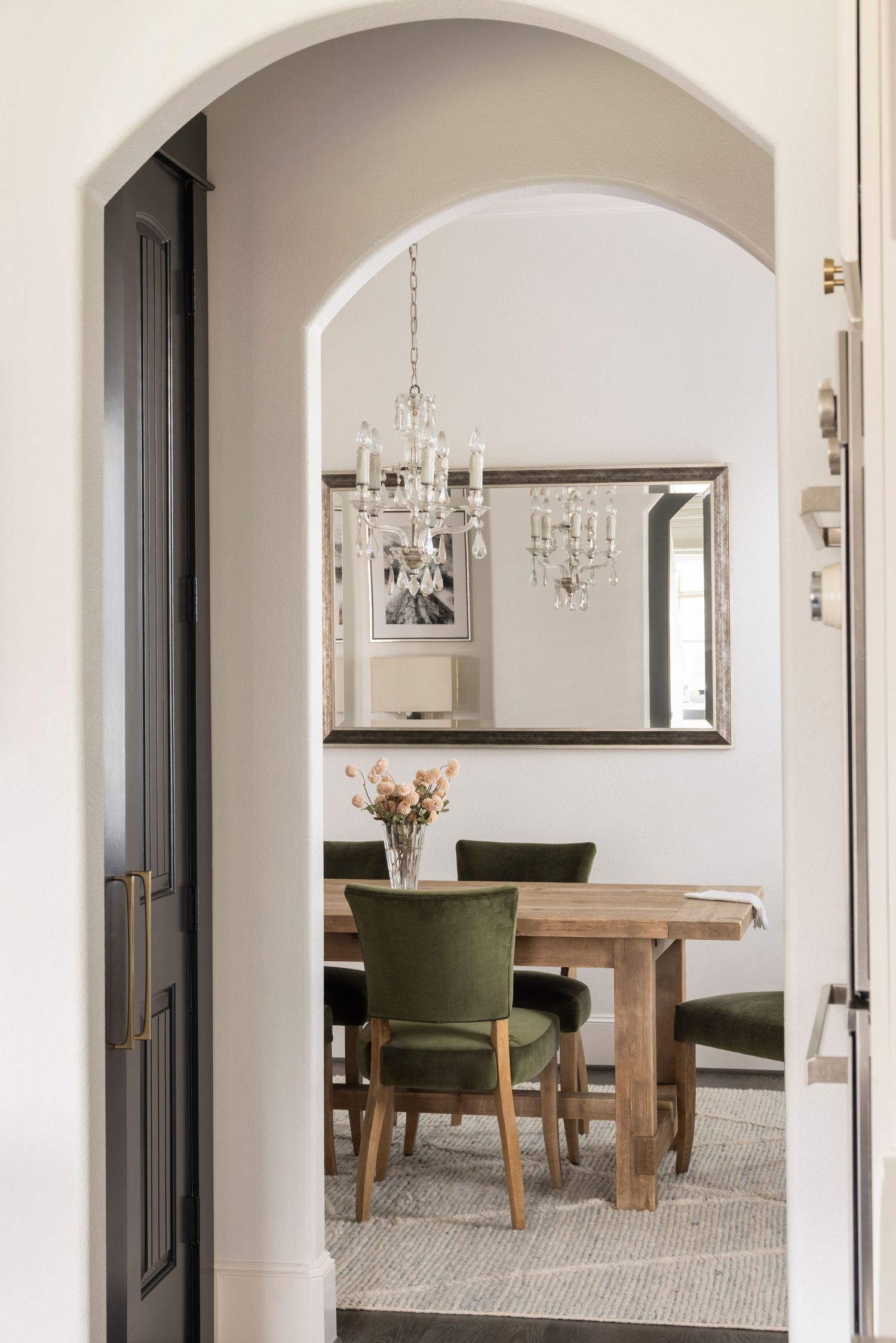Elegant dining room with arched doorways, crystal chandelier, wooden table, and green upholstered chairs on a neutral rug.