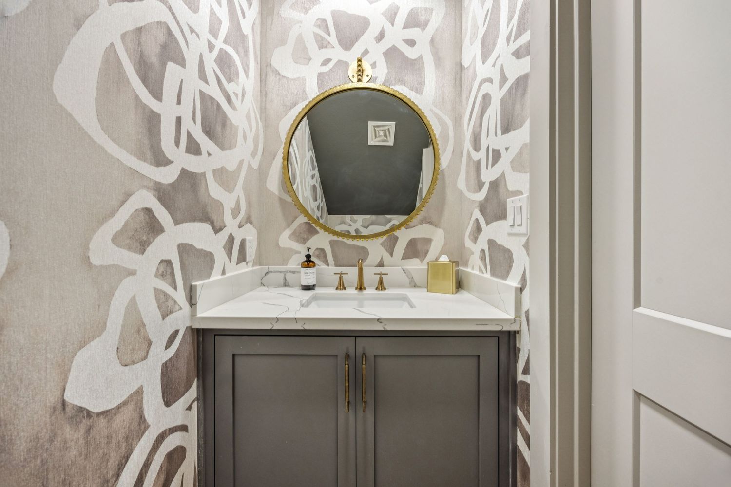 Elegant bathroom vanity with gold accents, circular mirror, and decorative wall patterns.