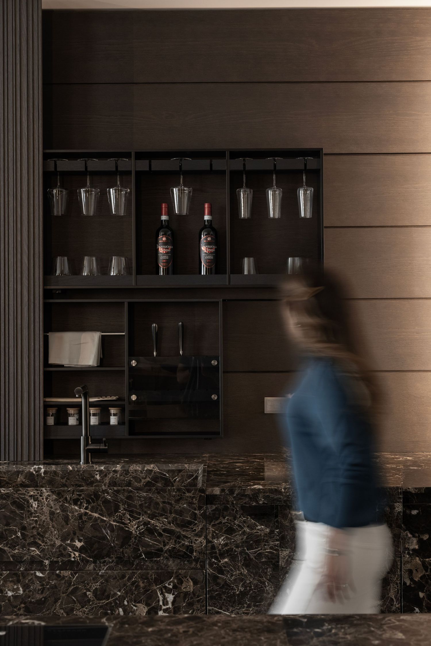 Modern bar area with dark marble countertop and wooden wall panels displaying glassware.