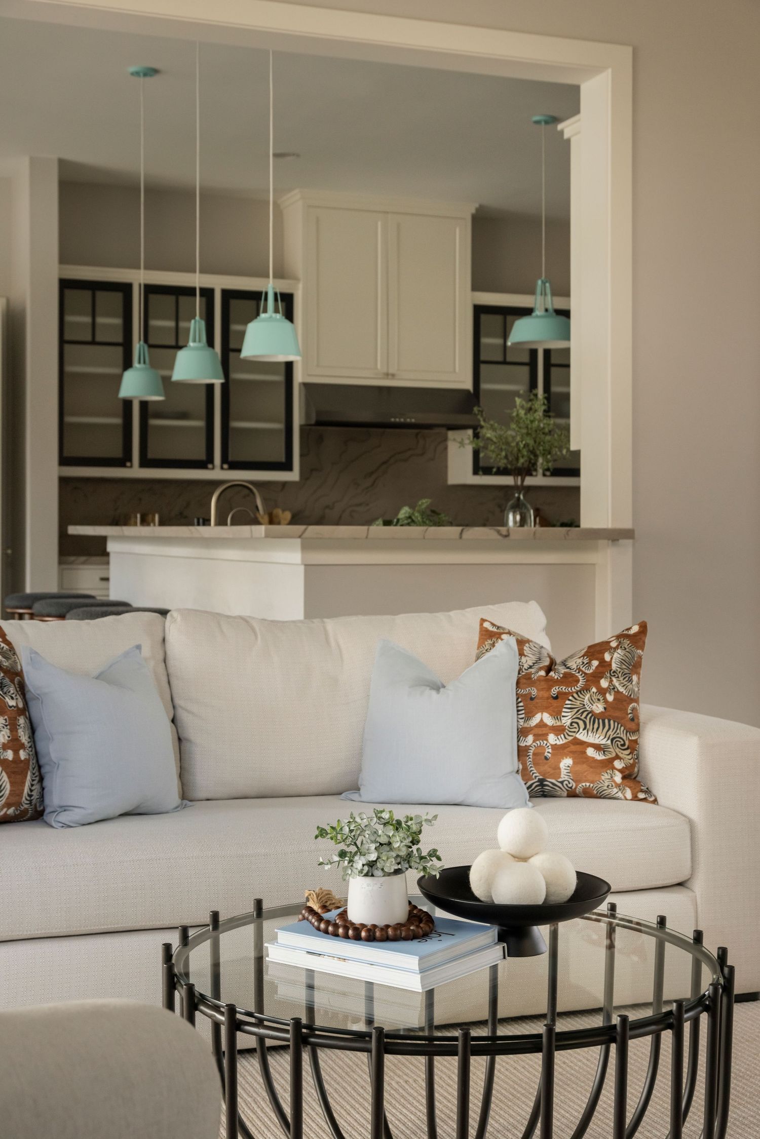 Open concept living space with white sofa, decorative pillows, and mint pendant lights in kitchen.