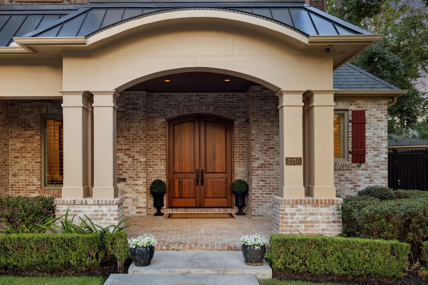 Luxurious home exterior featuring brick facade, wooden doors, and covered entry portico.