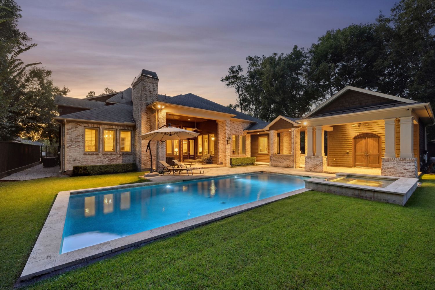 Twilight view of a luxury home's backyard featuring an illuminated pool and landscaping.