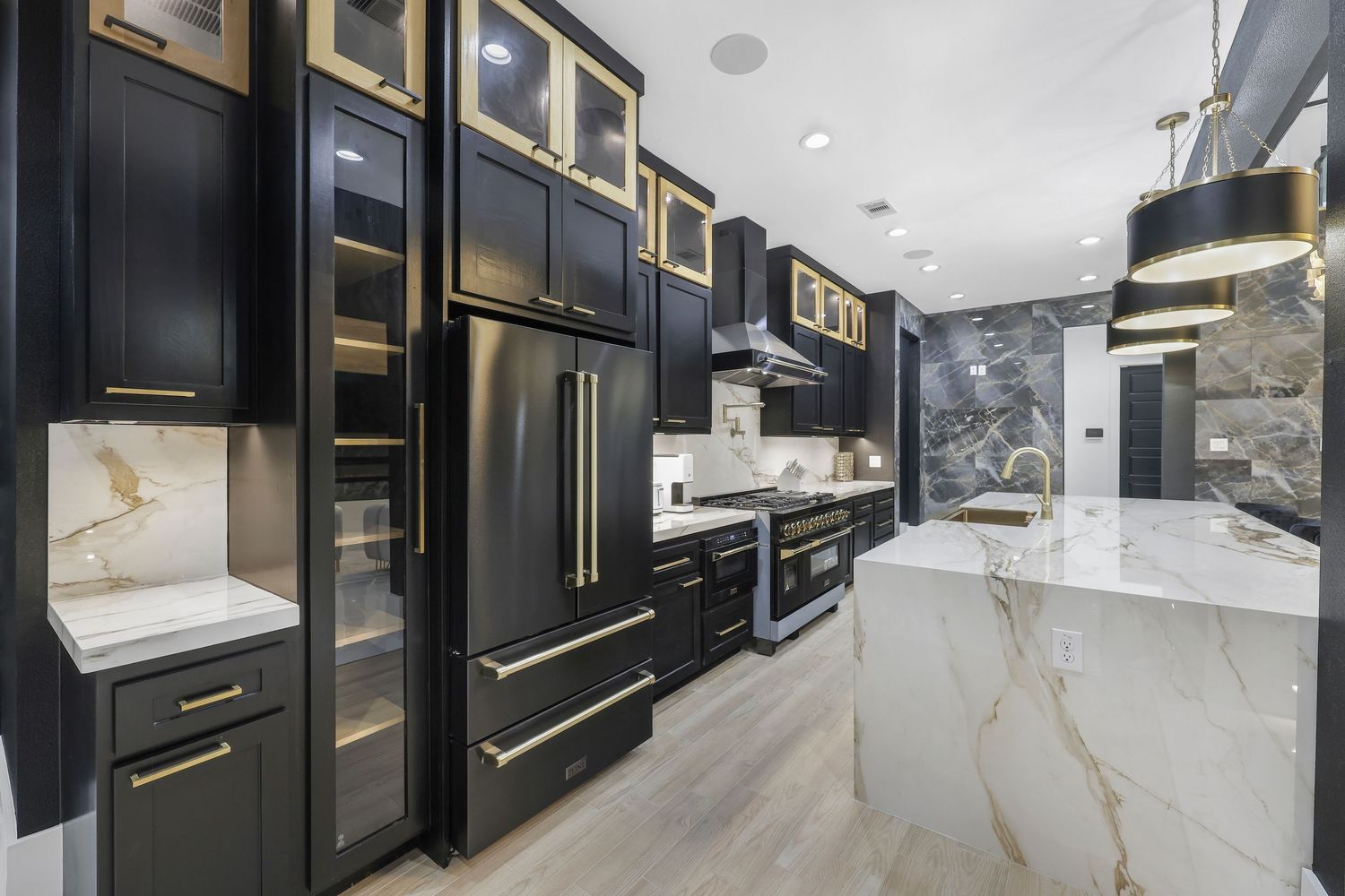 Modern black kitchen with gold hardware, marble countertops, and black stainless steel appliances.