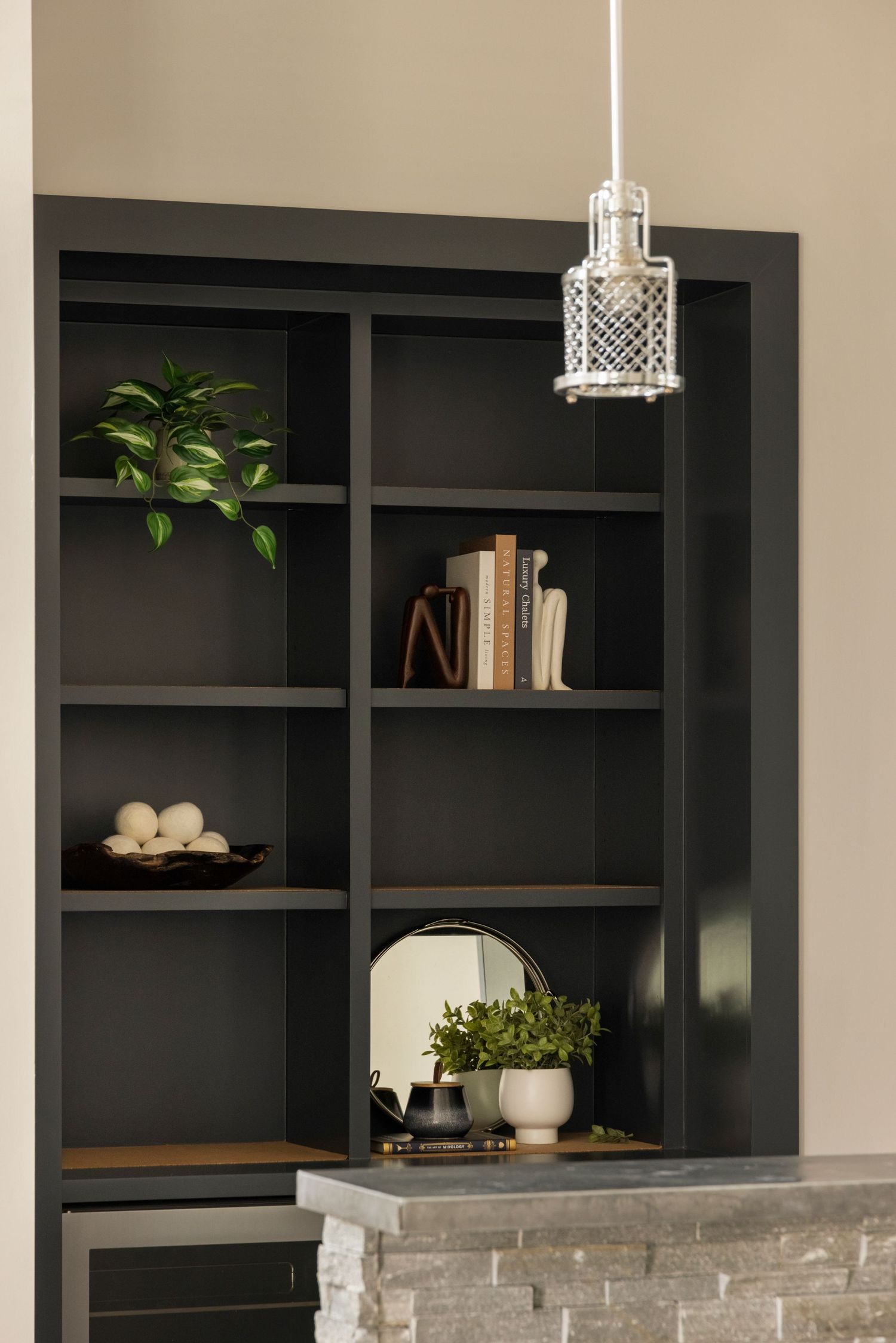 Black built-in shelving unit with decorative items and pendant lighting fixtures.