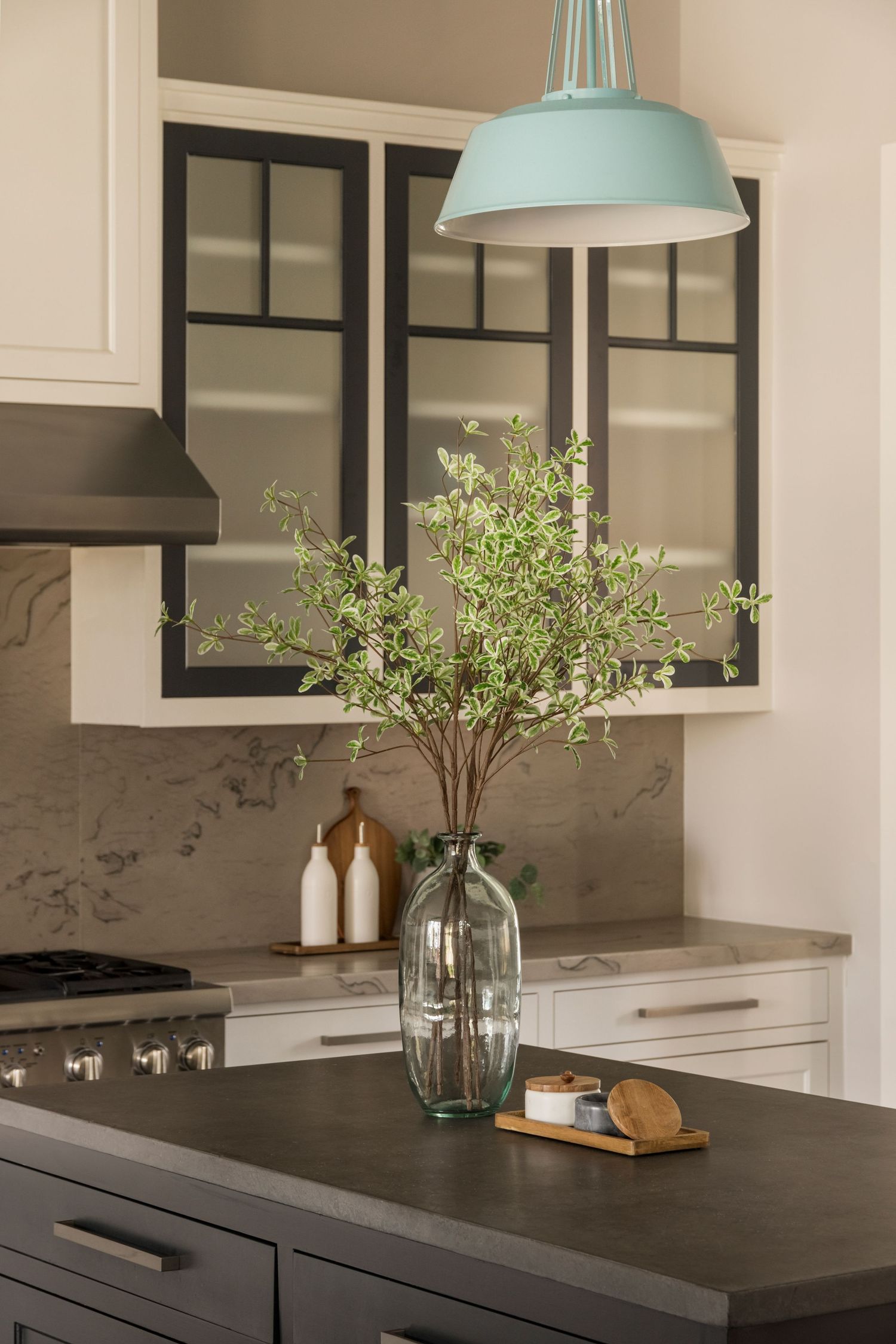 Contemporary kitchen featuring dark countertops, mint pendant lights, and glass vases with greenery.