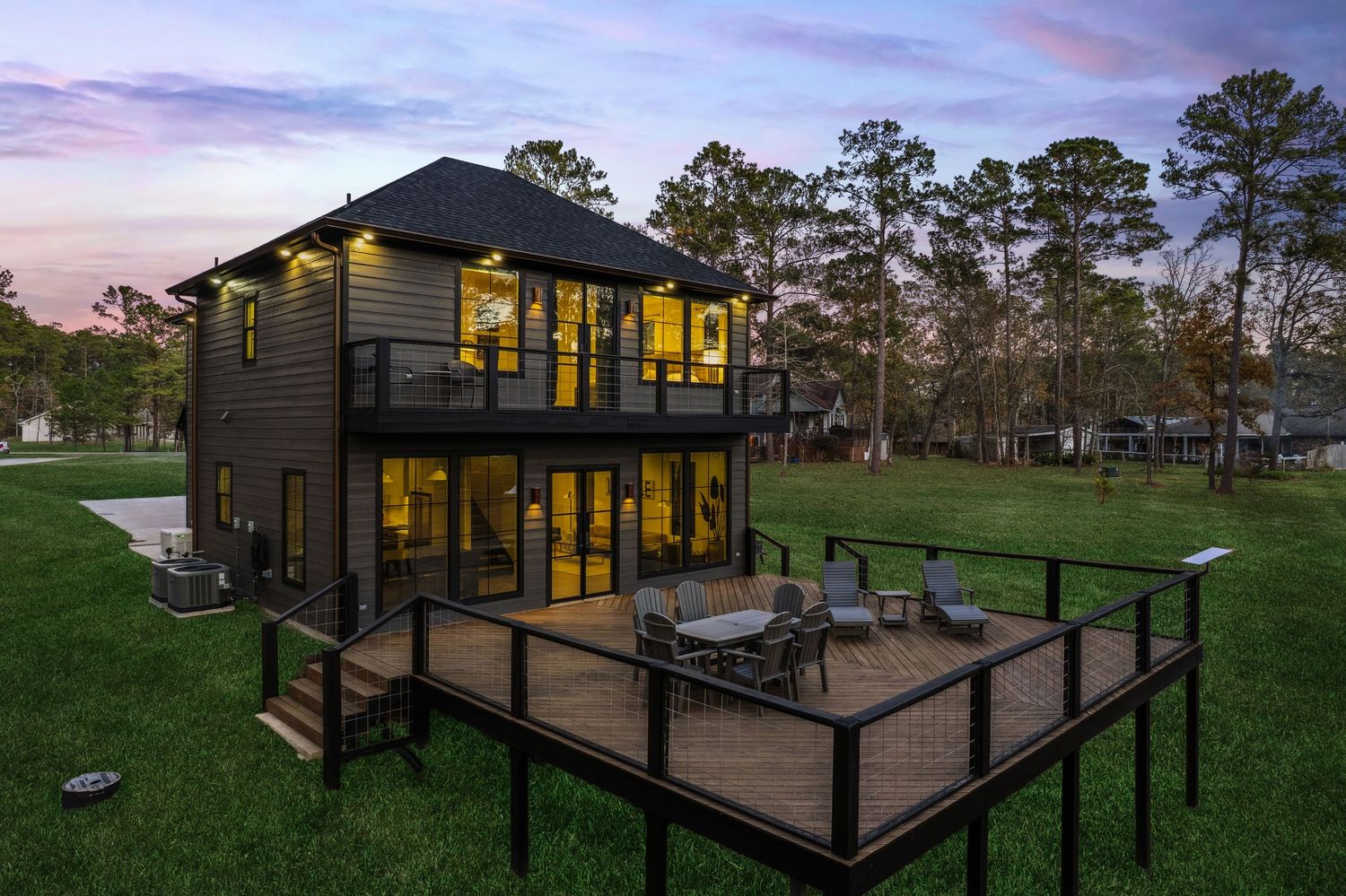 Modern black two-story house with expansive deck illuminated at twilight.