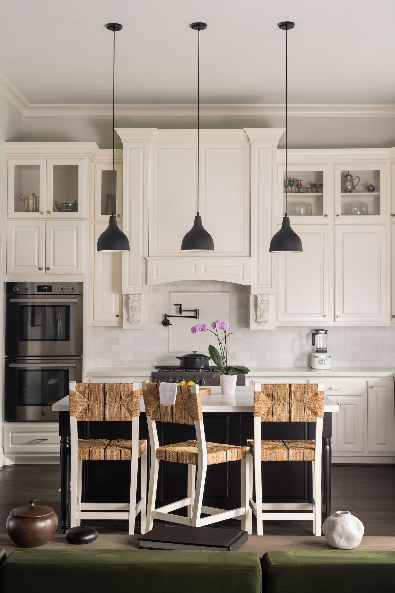 Modern white kitchen with black pendant lights and natural wood counter stools along a white island.