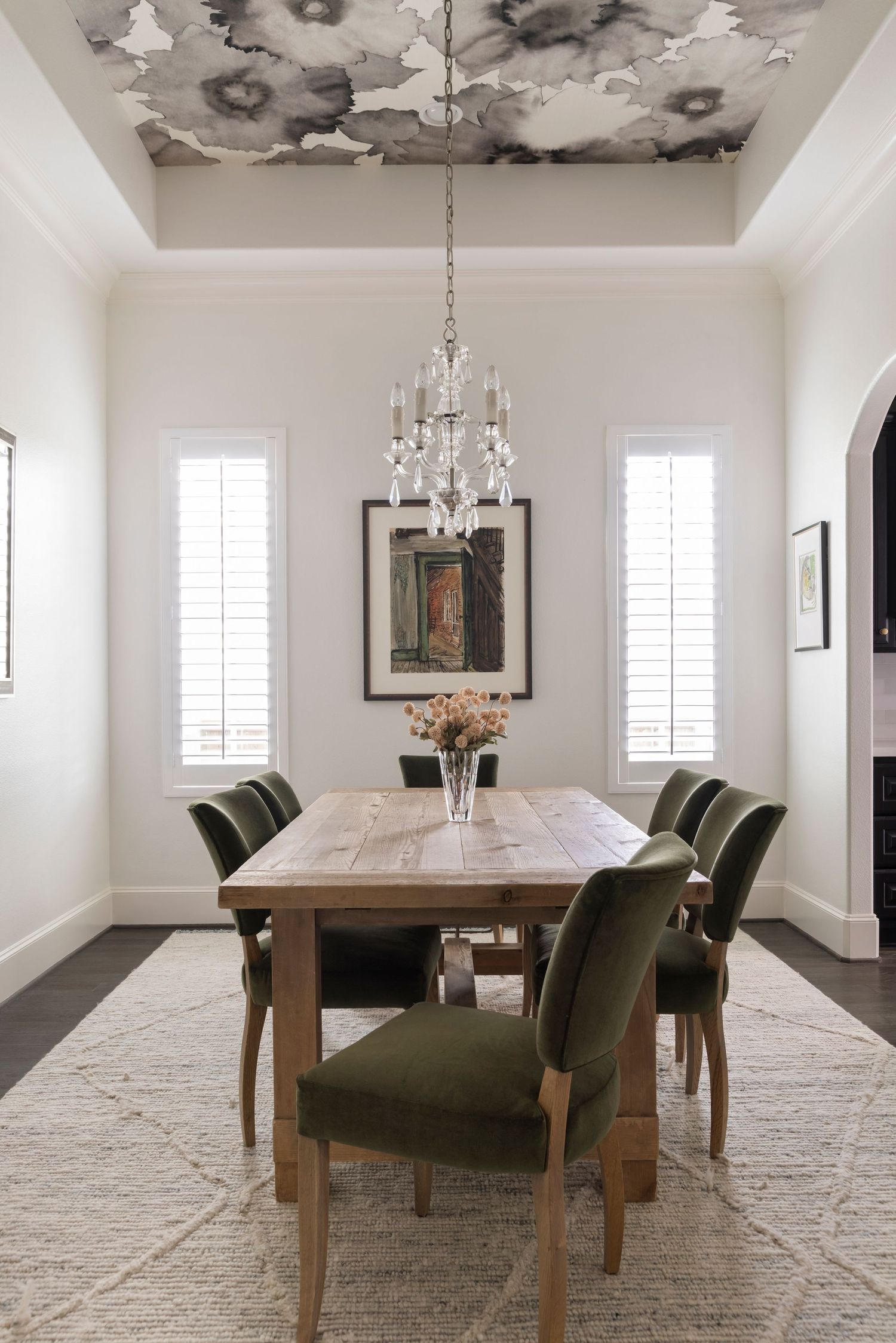 Elegant dining room featuring a long wooden table with dark green upholstered chairs and crystal chandeliers.
