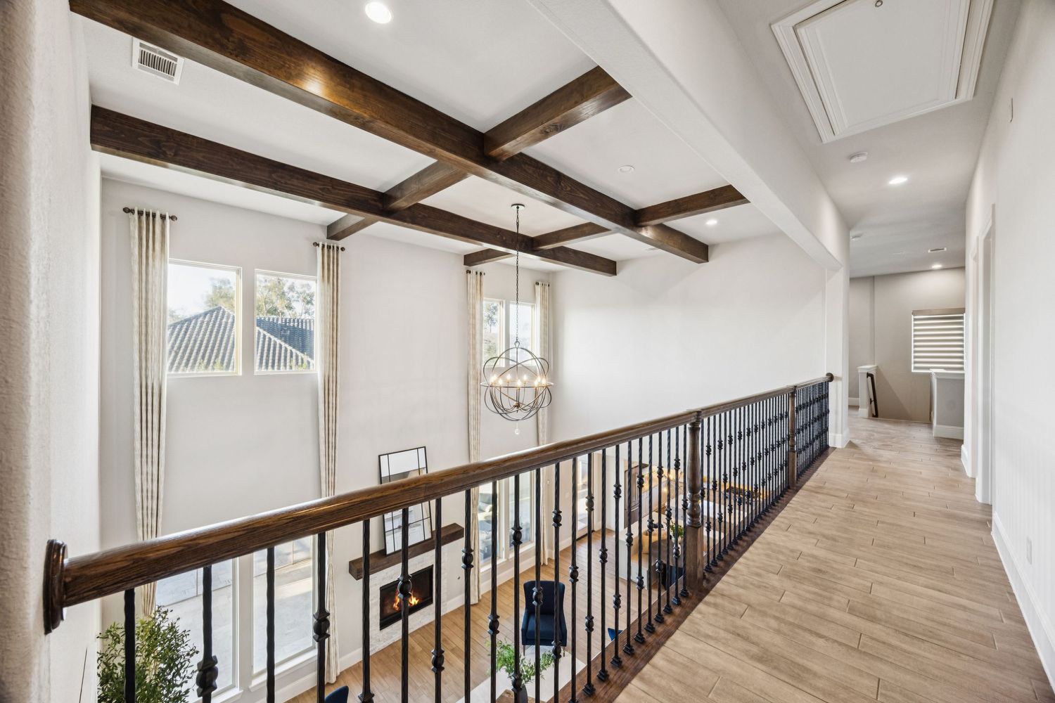 Elegant upstairs hallway with exposed wooden beams, white walls, and black metal railings overlooking the lower level.