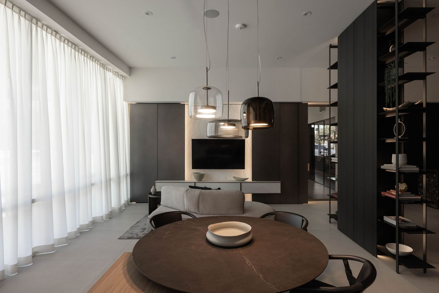 Elegant dining area with round wooden table and pendant lighting in minimalist setting.