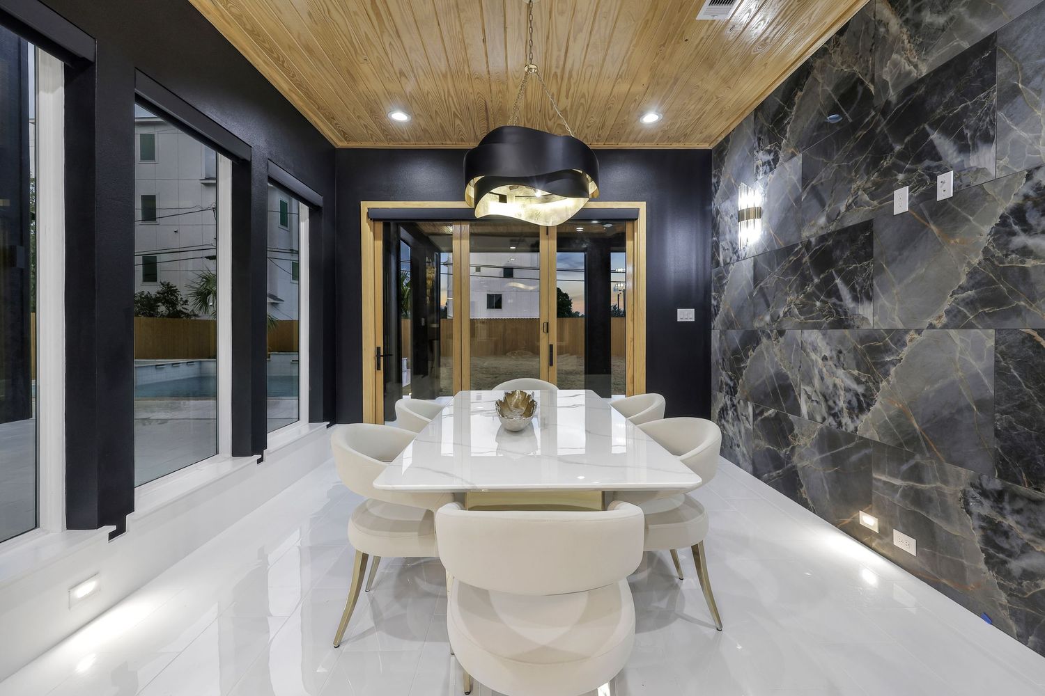 Sophisticated dining room with white marble table, black accent wall, and wooden ceiling detail.