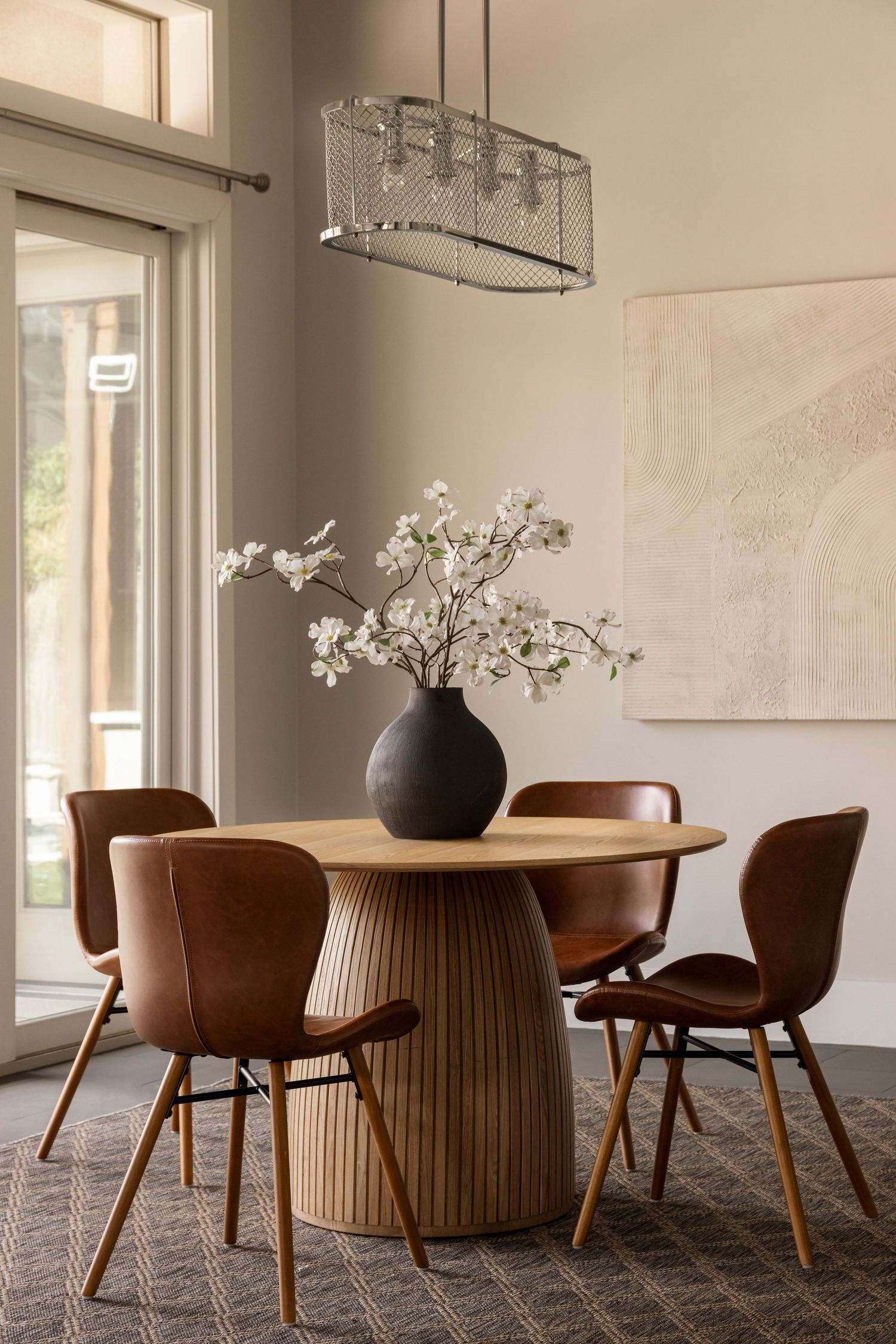 Elegant dining area featuring round wooden table, brown leather chairs, and white floral centerpiece.