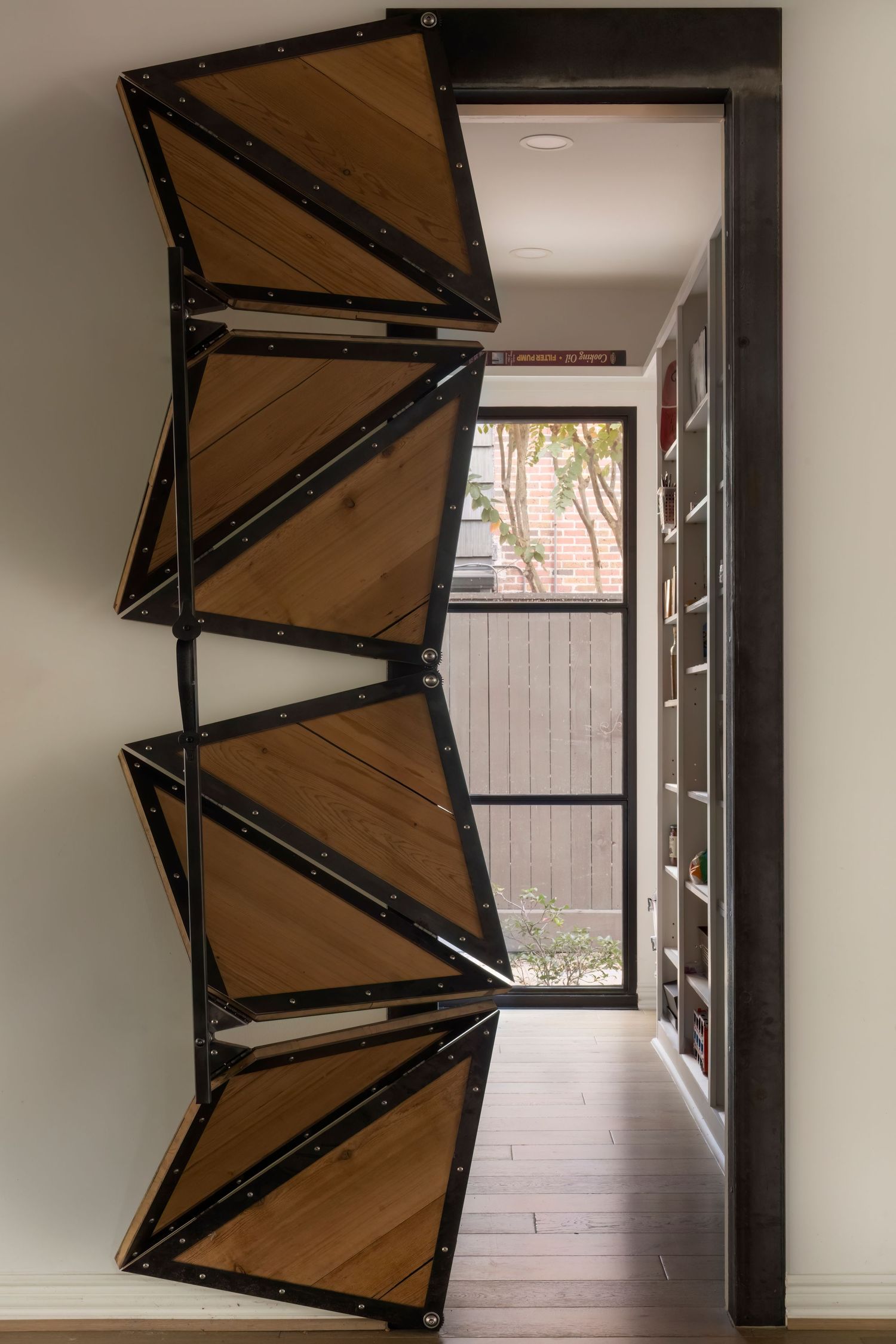 Unique folding wooden door panels with black metal frames in modern hallway design.