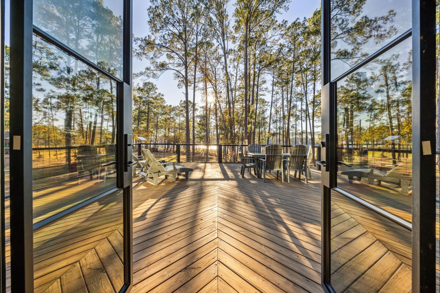 Chevron pattern wooden deck with glass doors framing pine forest view at sunset.
