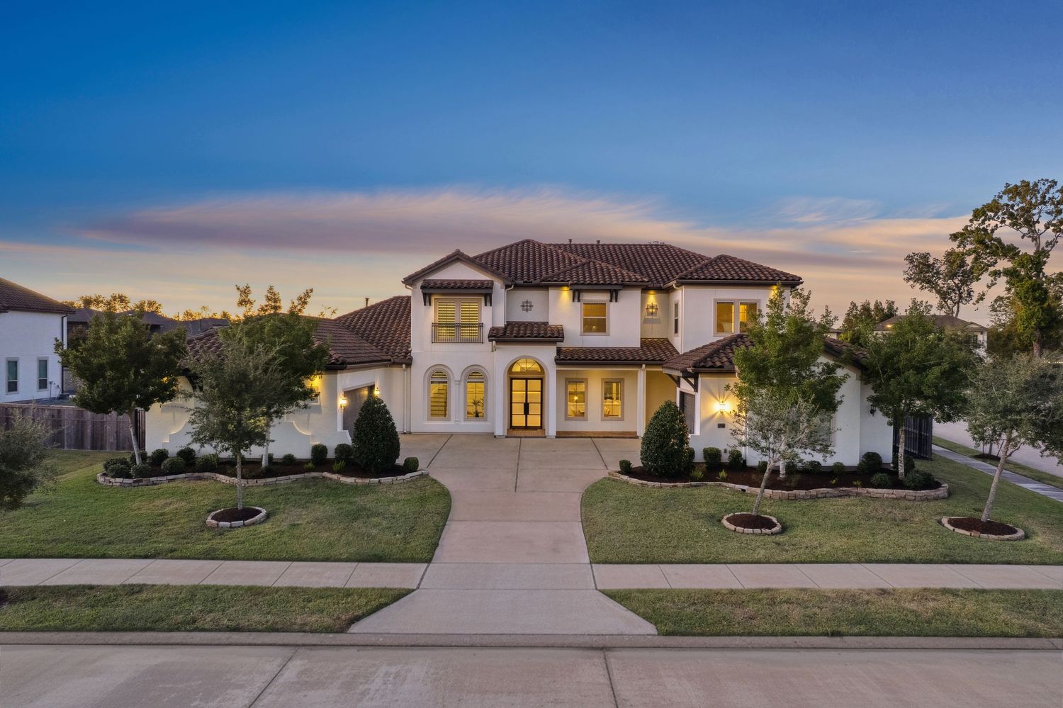 Elegant white Mediterranean-style mansion with landscaped front yard at dusk.