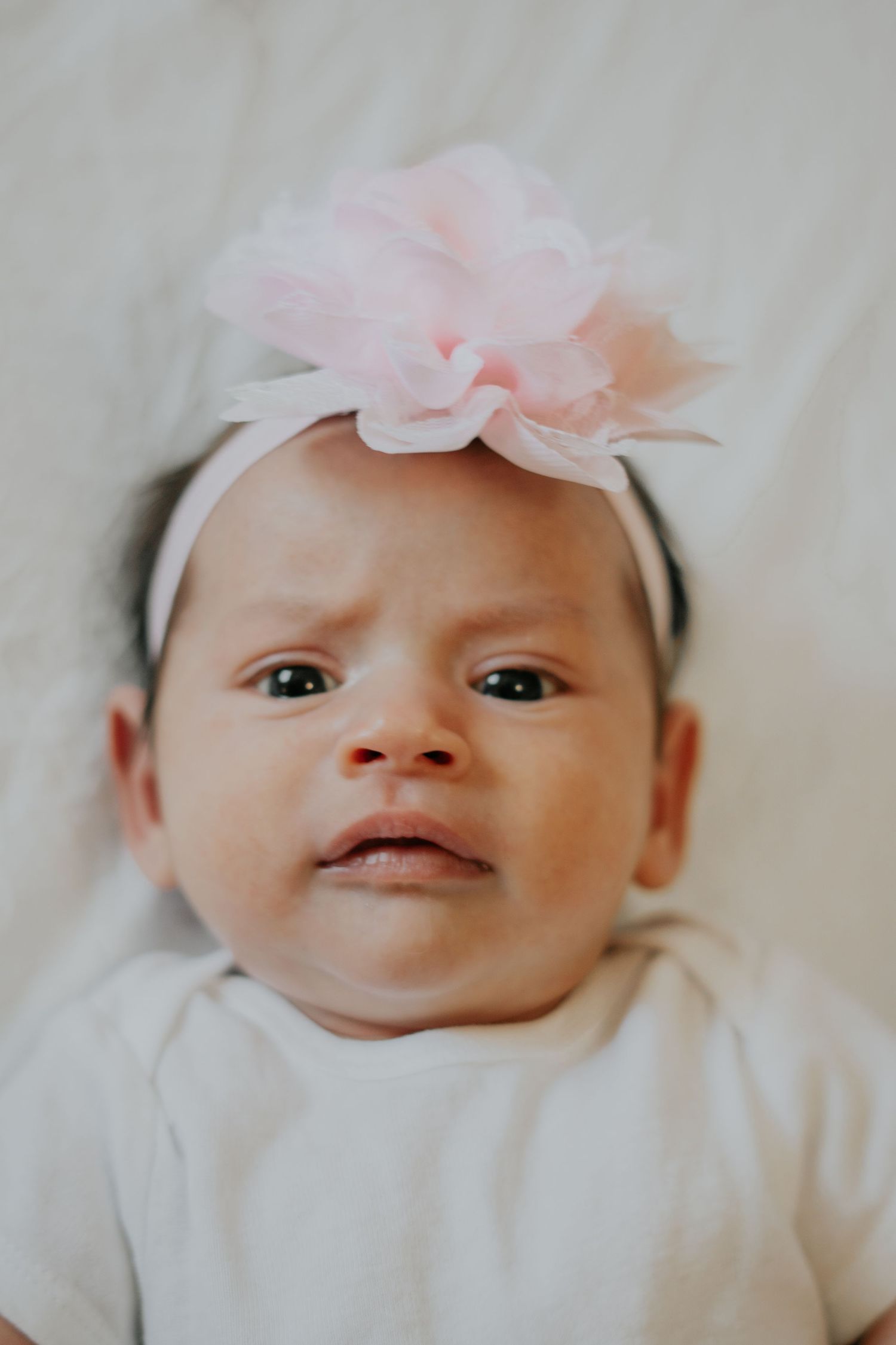 Adorable newborn baby girl wearing a pink flower headband lying on a white background.