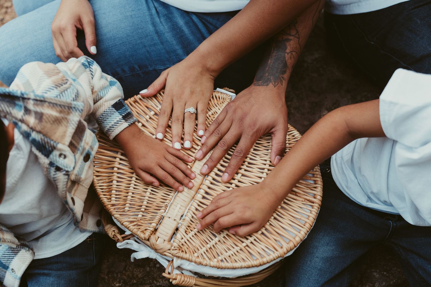 Close-up of multiple hands resting together on a wicker basket lid outdoors.