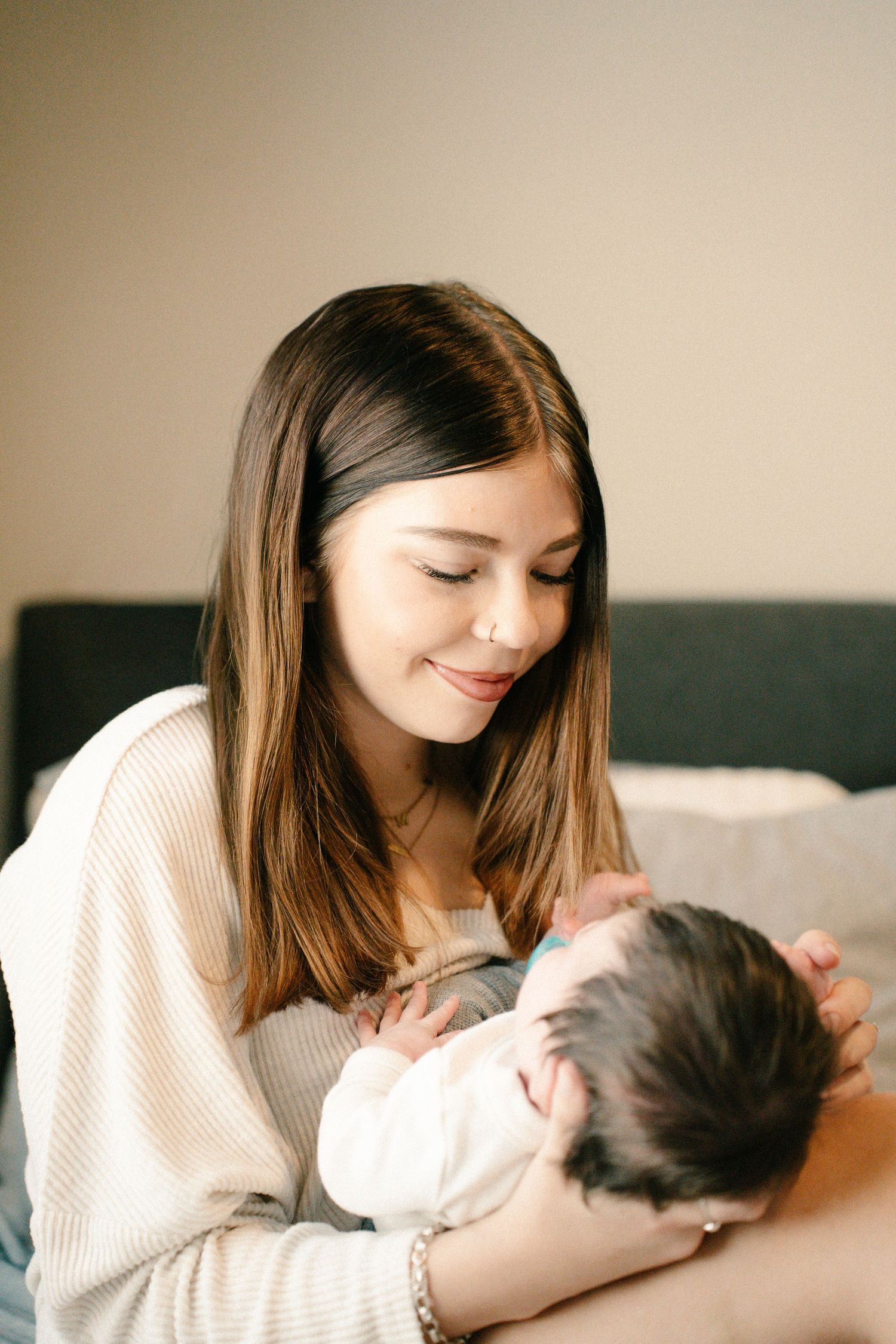 Young mother smiling tenderly while cradling her newborn baby in her arms indoors.