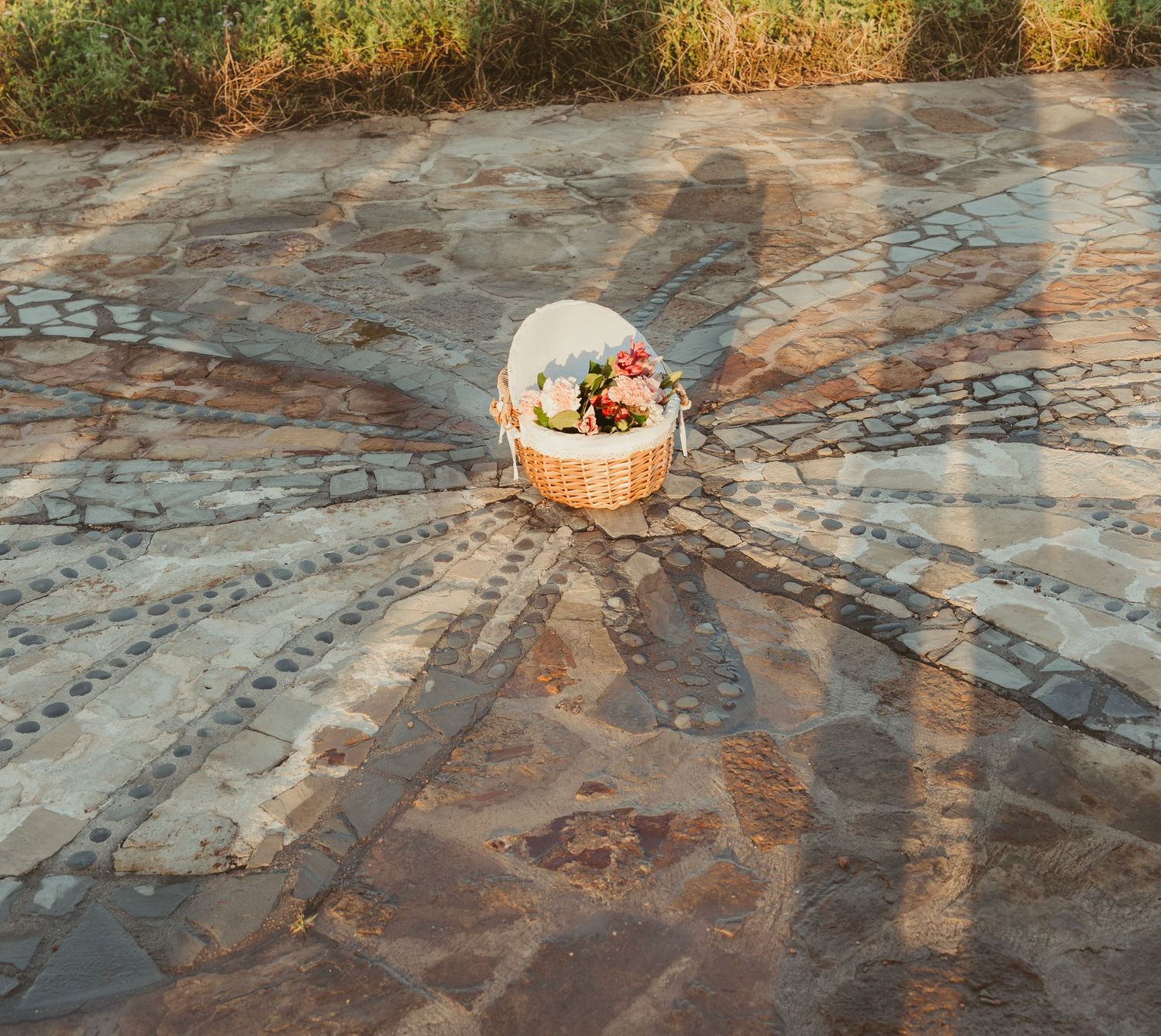 A wicker basket filled with colorful flowers sits on a decorative stone mosaic pathway.