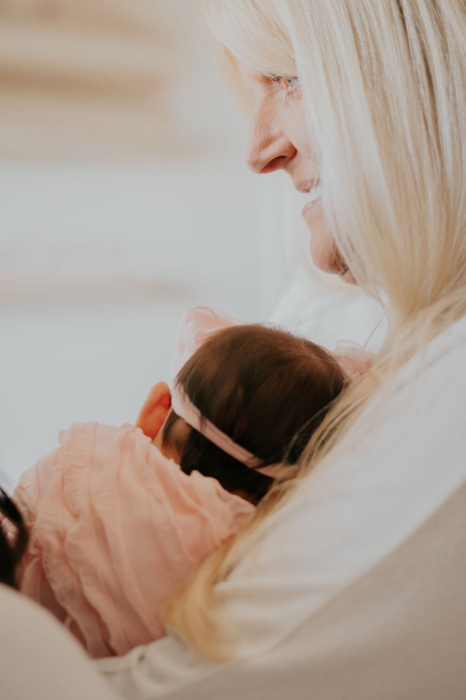Blonde woman tenderly cradling a sleeping newborn baby dressed in pink during a family session.