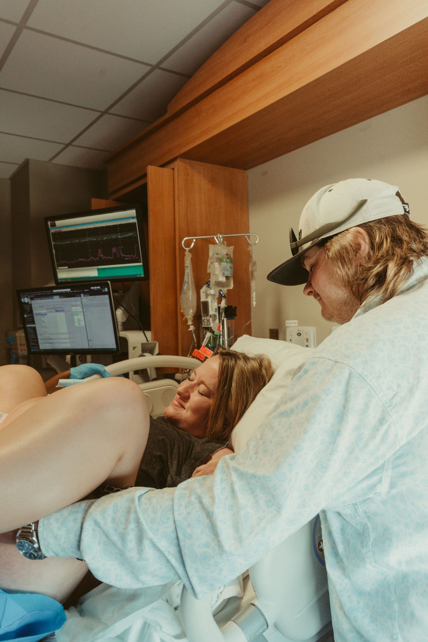 Woman in labor at hospital bed supported by partner during childbirth delivery.