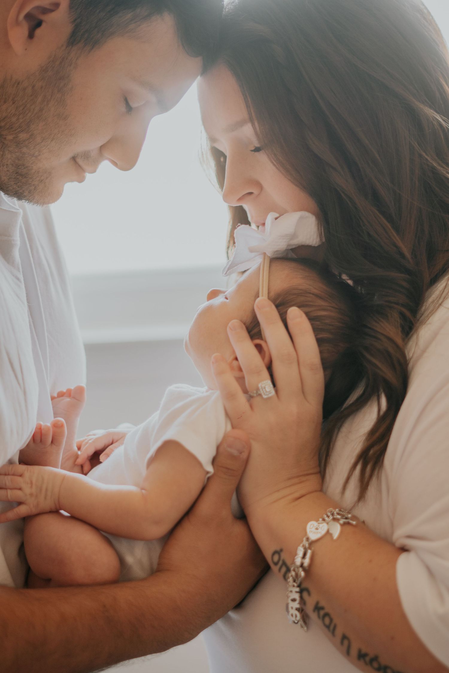 New parents leaning in together smiling at their newborn baby during an intimate family photo.