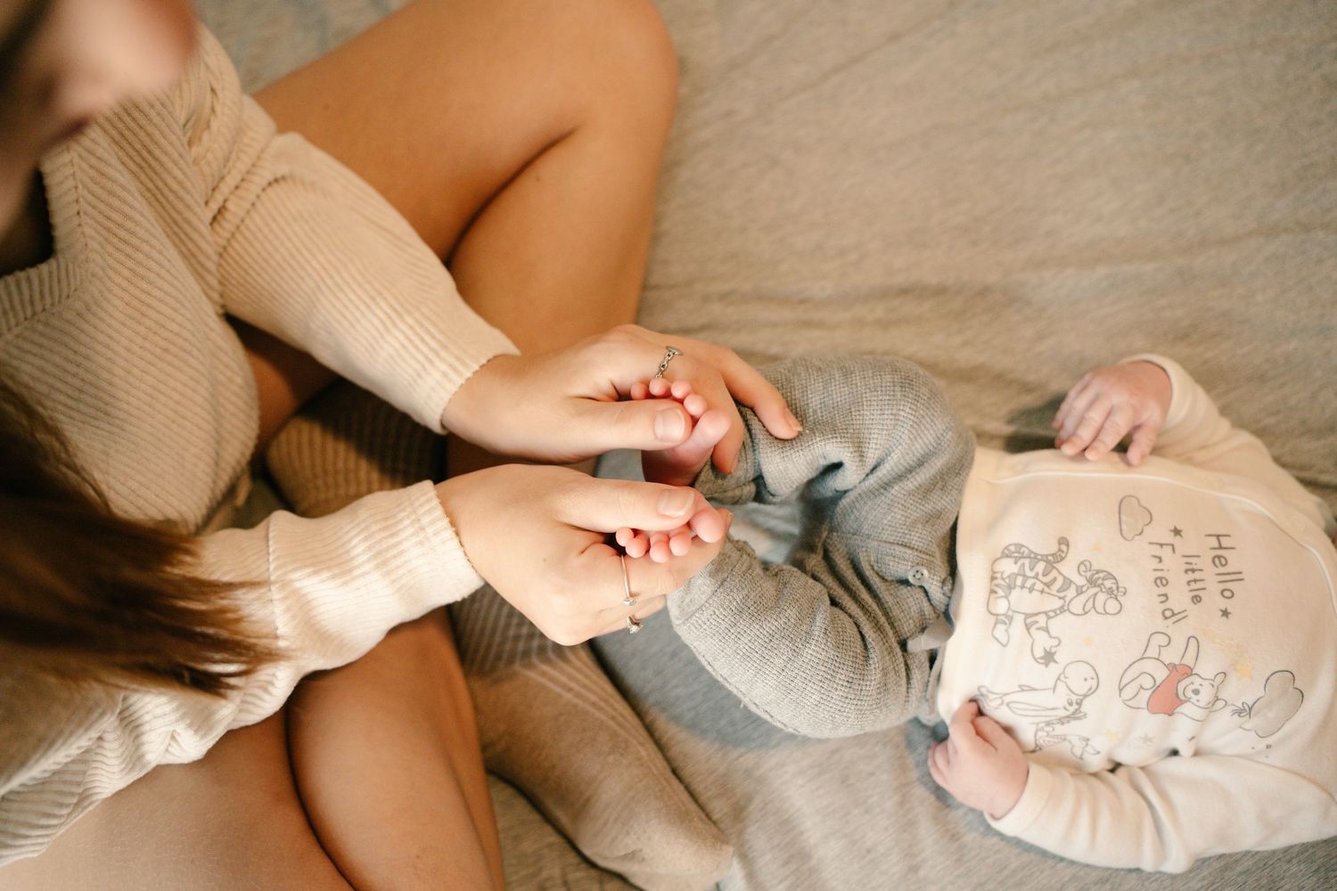Mother gently holding her newborn baby's feet while sitting together on a soft bed.