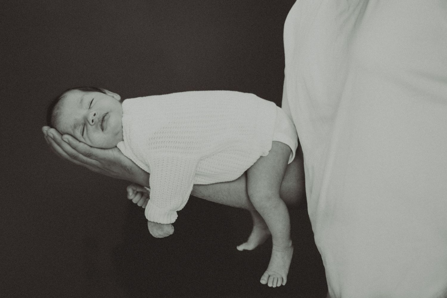 Black and white photo of a newborn baby being held in one hand during a portrait session.