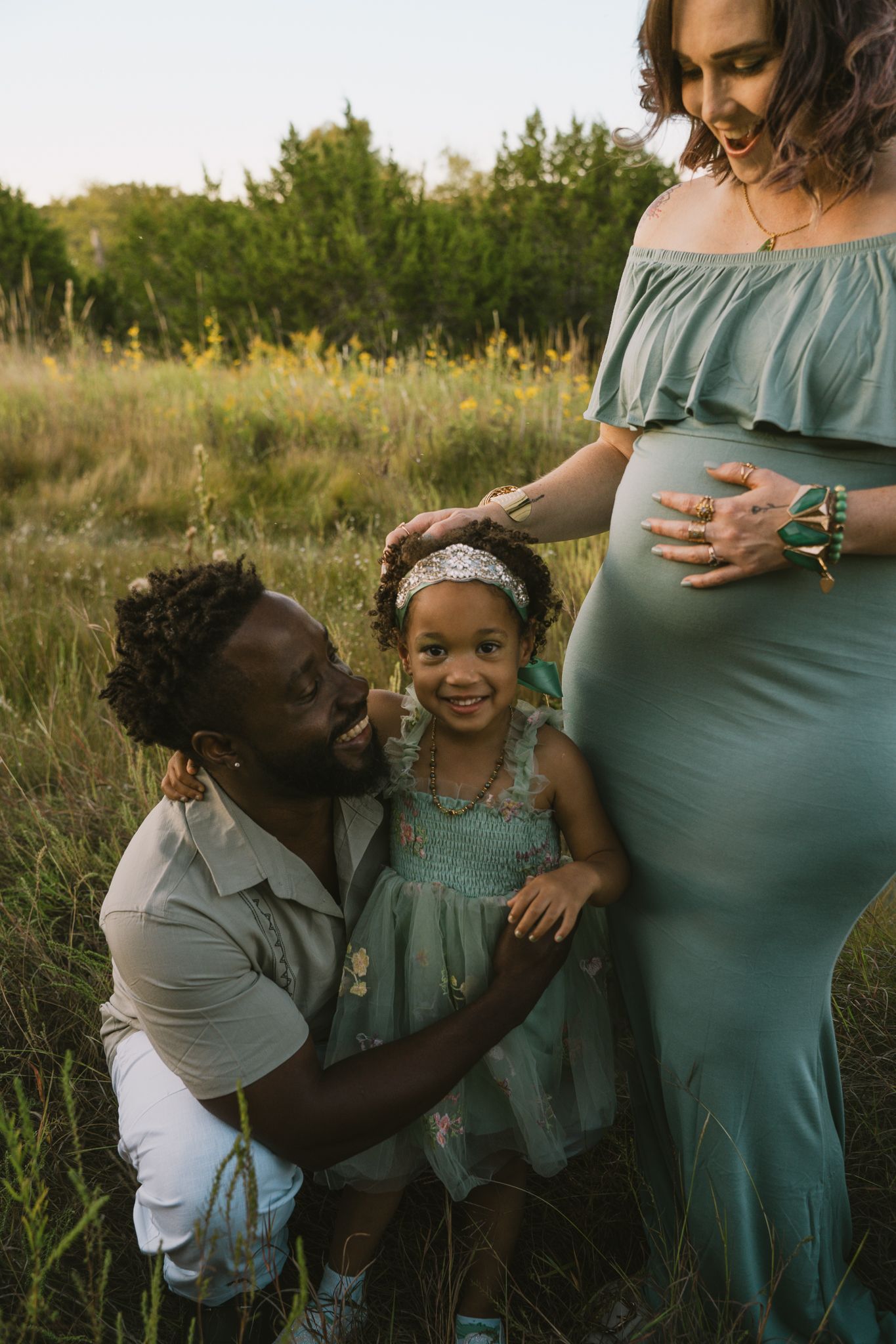 Interracial family maternity photo with father, daughter, and pregnant mother in teal gown.