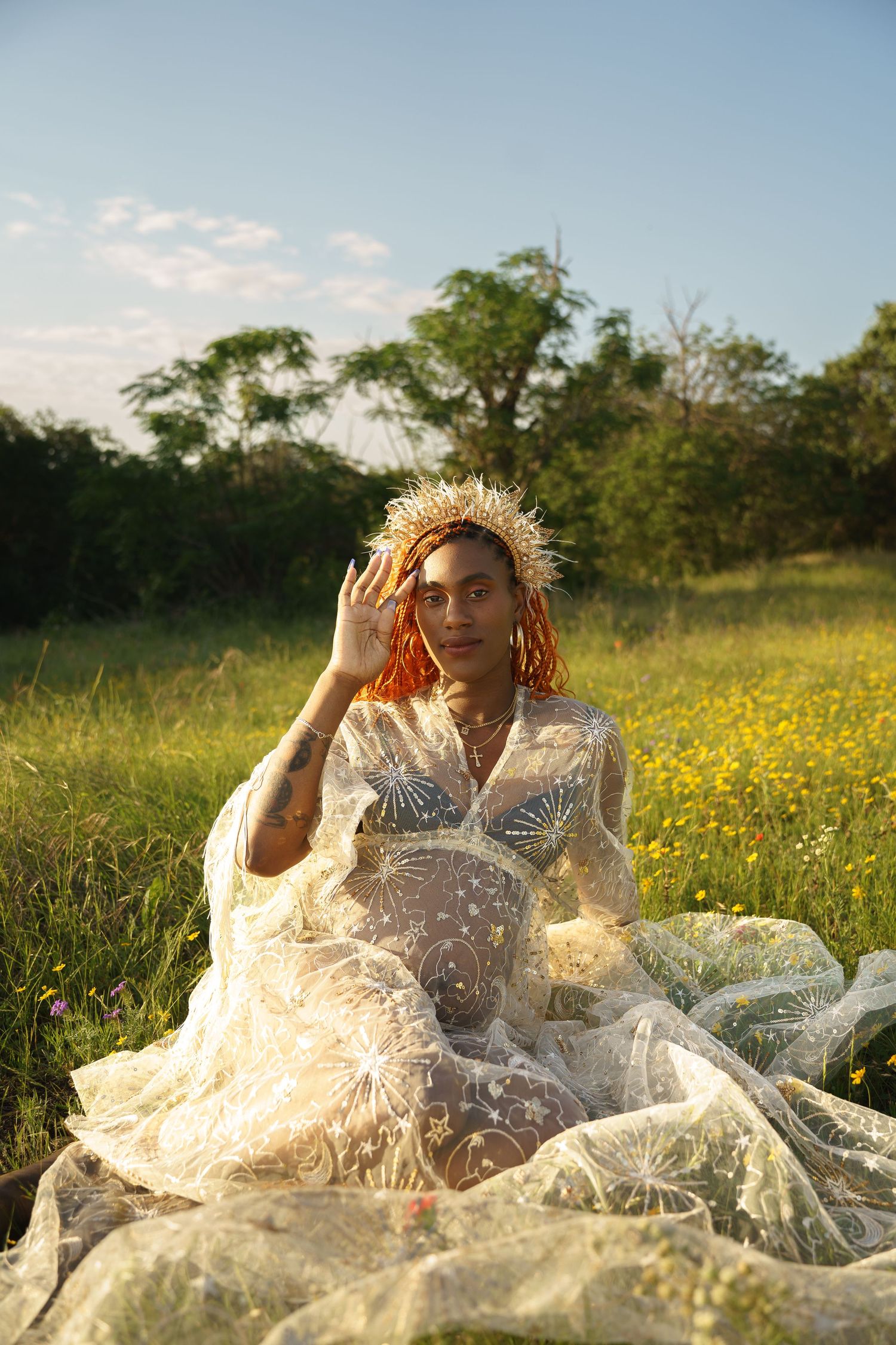 Pregnant woman in a celestial lace dress sitting in a wildflower field on a sunny day.