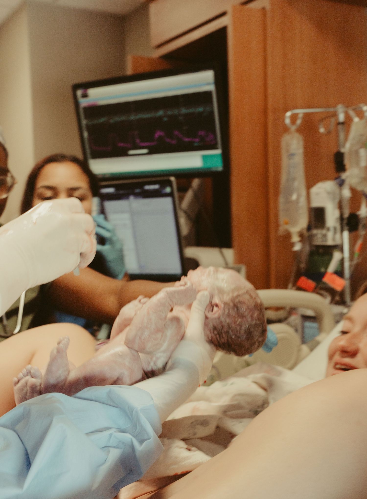 Medical staff hold a newborn baby immediately after delivery in a hospital room.