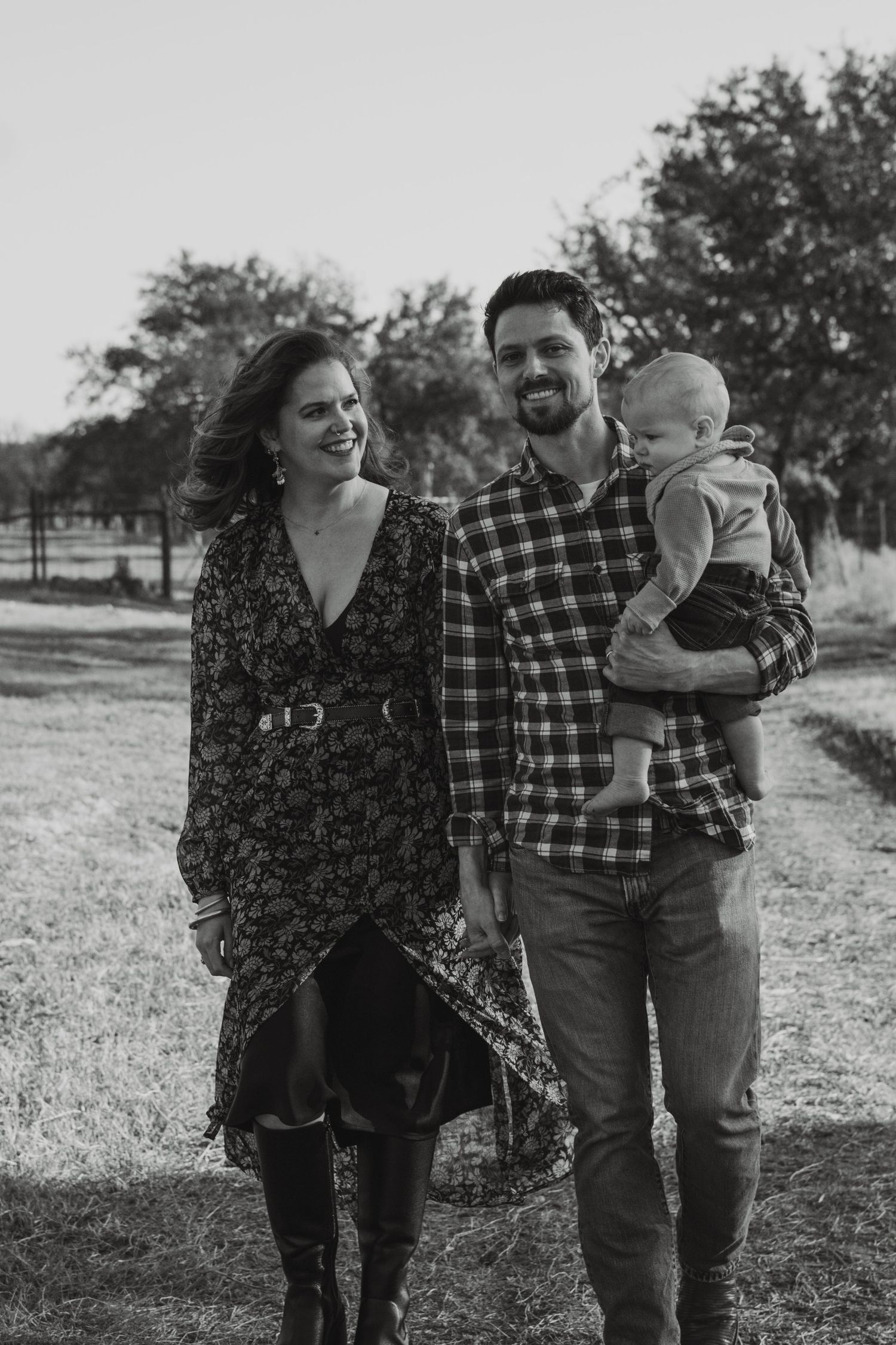 Black and white portrait of smiling family with father holding baby in plaid shirt outdoors.