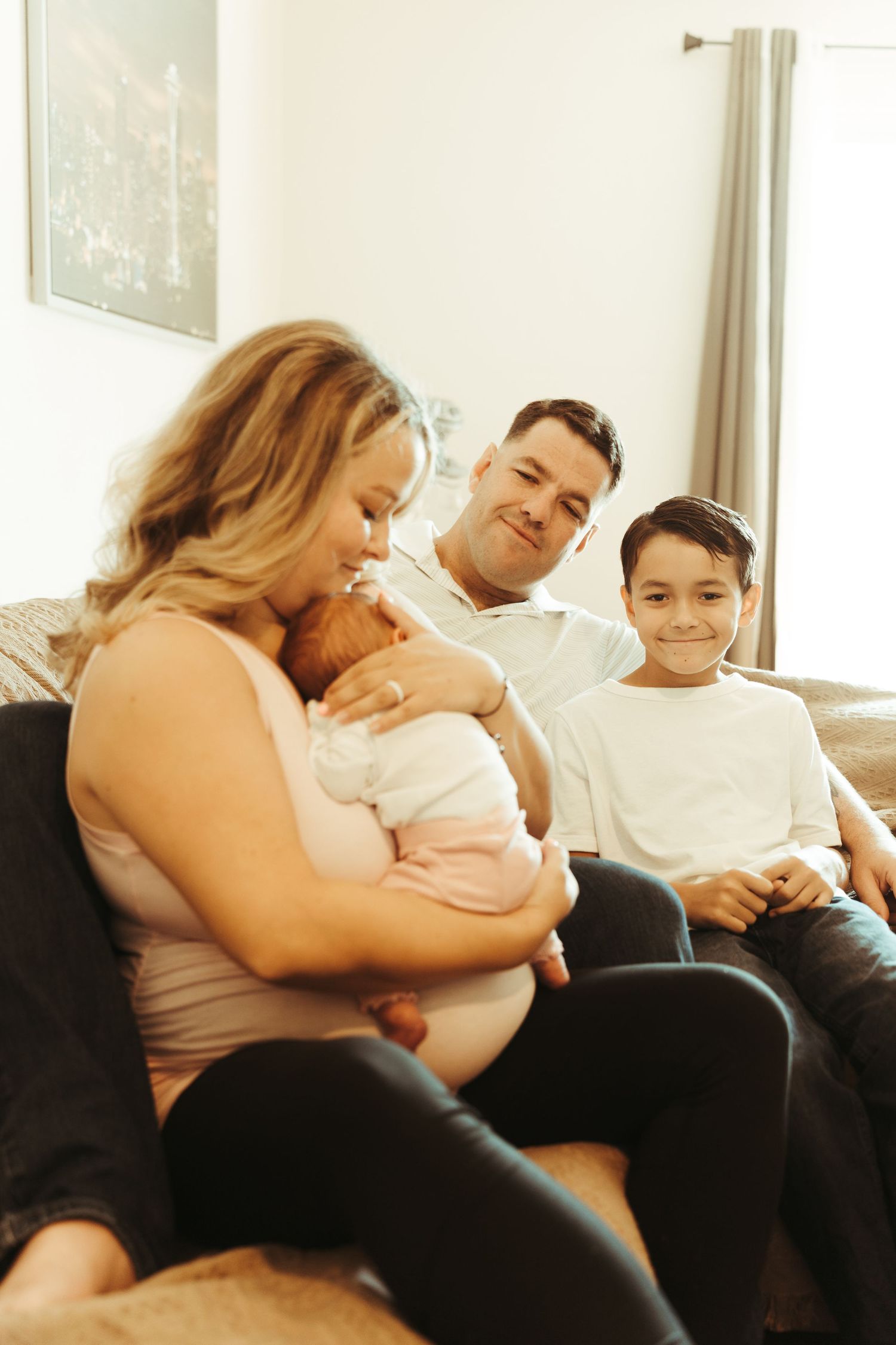 A happy family with a newborn baby and young son relaxes together on a cozy living room sofa.